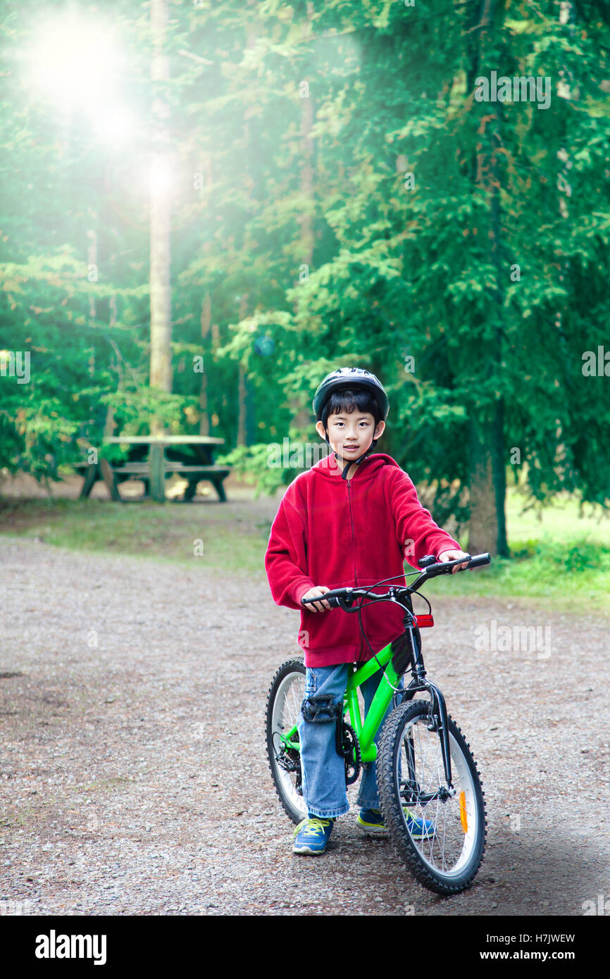An Asian boy riding his bike in an outdoor park. Backlit by morning sunlight in background with deliberate lens flare for effect Stock Photo