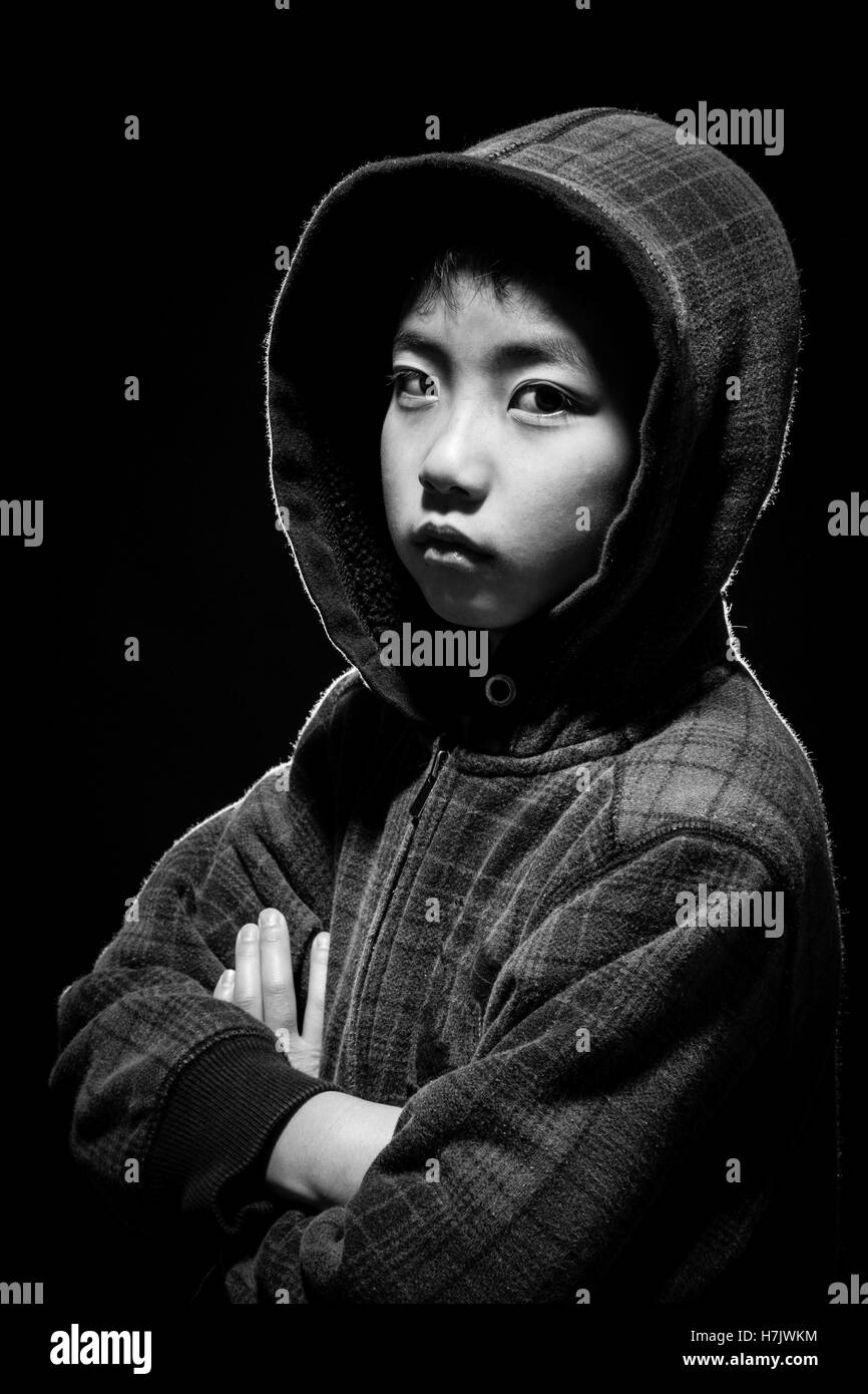 Asian boy in hoodie jacket staring at camera. Black and white shot in studio with back lighting for highlights. Stock Photo