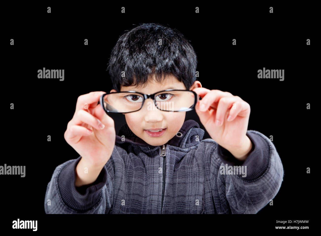 Cute Asian boy holding and looking through his eyeglasses, magnifying his eyes in the process. Stock Photo