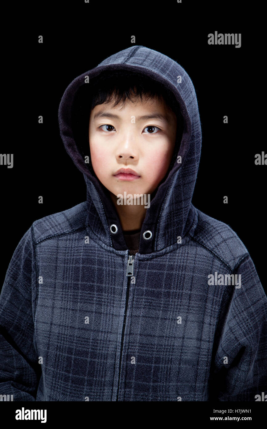 Cute Asian boy wearing hooded sweatshirt posing in studio. Isolated on black. Stock Photo