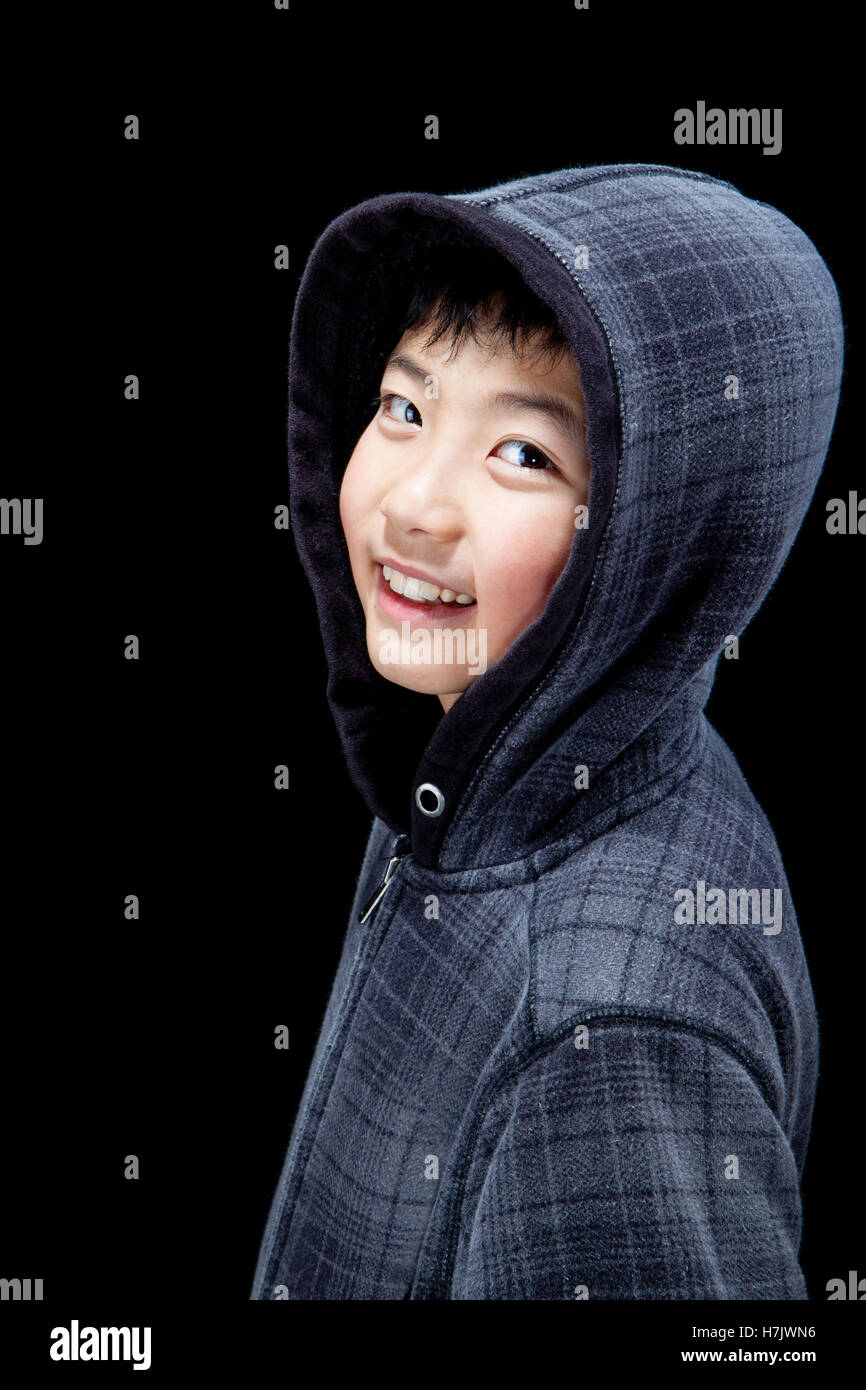 Cute Asian boy wearing hooded sweatshirt posing in studio. Isolated on black. Stock Photo