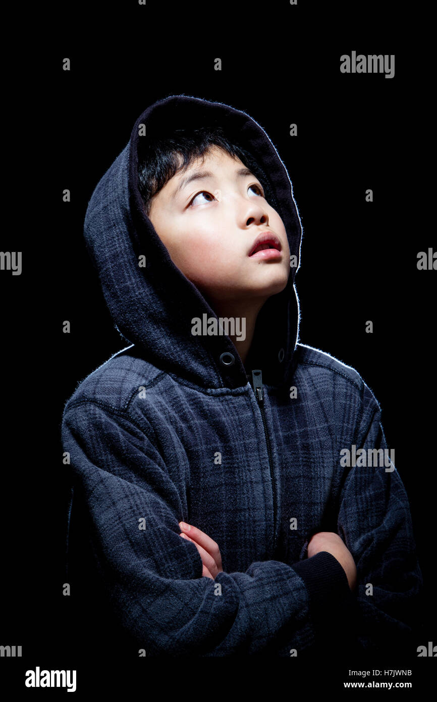 Cute Asian boy wearing hooded sweatshirt posing in studio. Isolated on black. Stock Photo