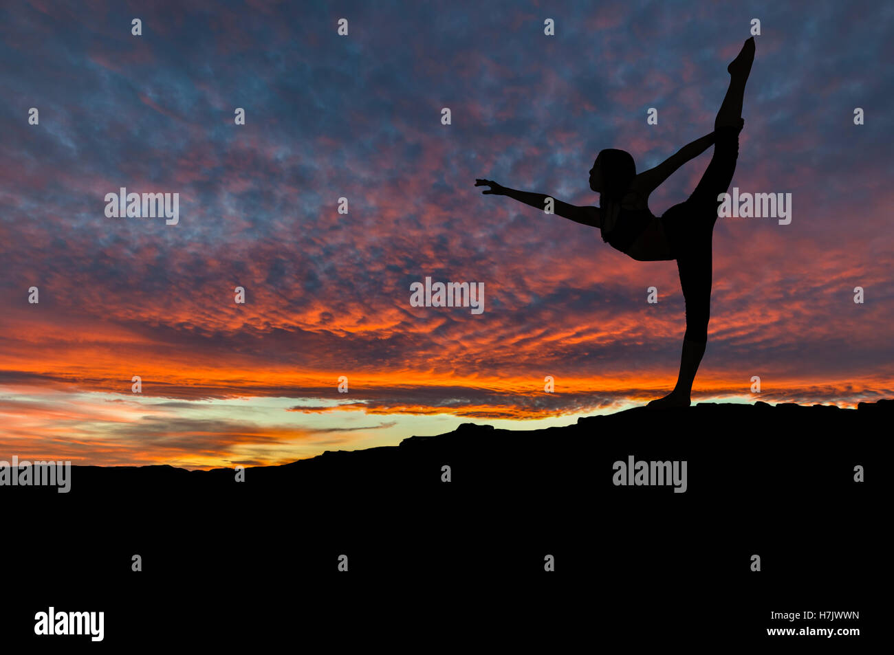 Silhouette of woman dancing and exercising on mountain top with sunset sky in the background. Stock Photo