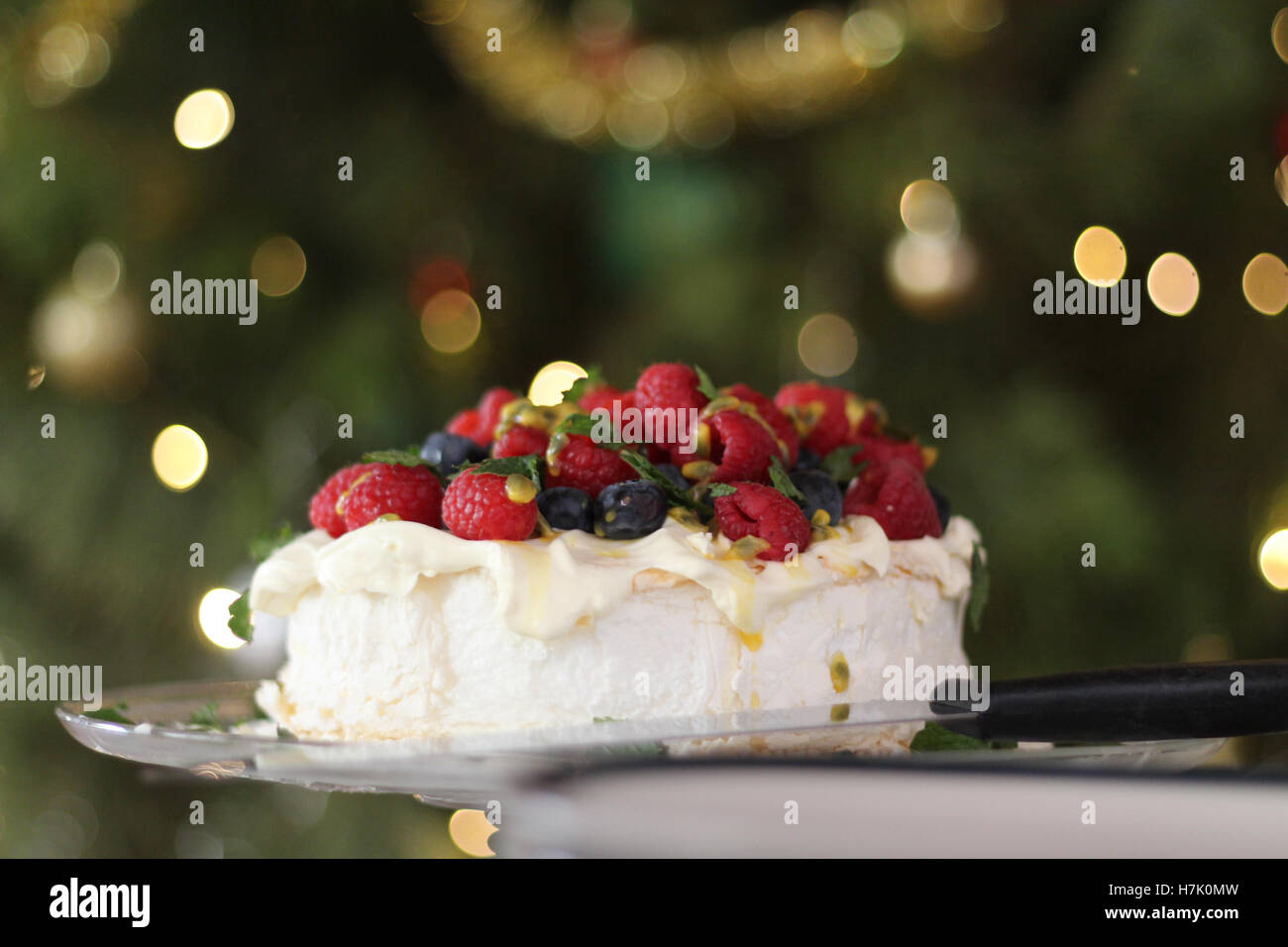 Pavlova with cream & berries, Australian dessert. In the background is the Christmas tree with fairy lights and baubles. Stock Photo