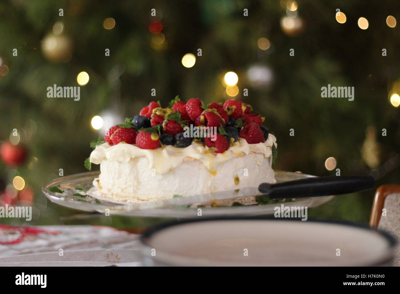 Pavlova with cream & berries, Australian dessert. In the background is the Christmas tree with fairy lights and baubles. Stock Photo