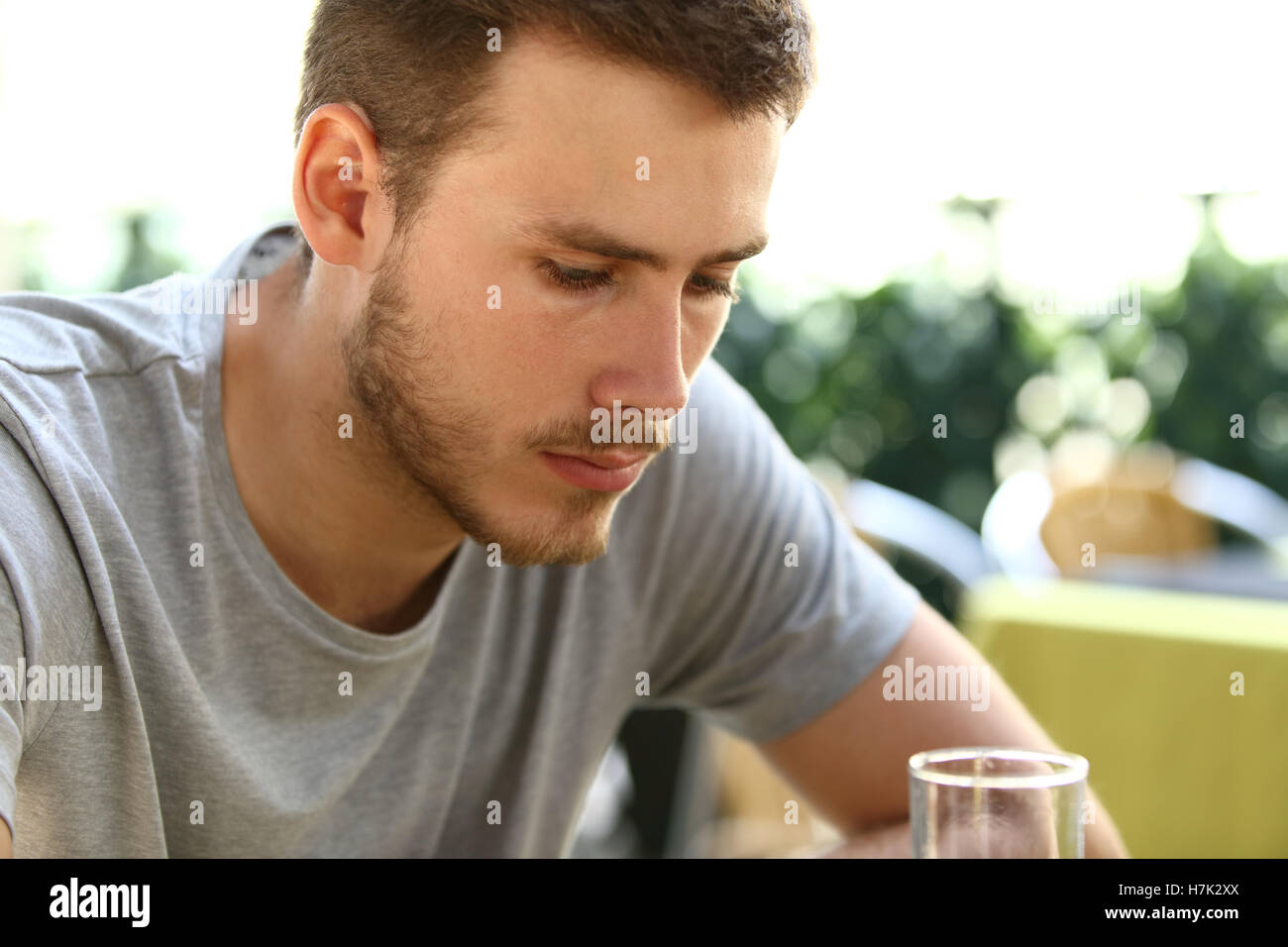 Portrait of a very sad single man sitting alone and drinking outside in a restaurant terrace Stock Photo