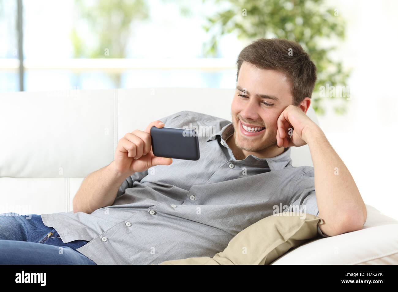 Happy guy enjoying watching entertainment content on a phone sitting on a couch at home Stock Photo