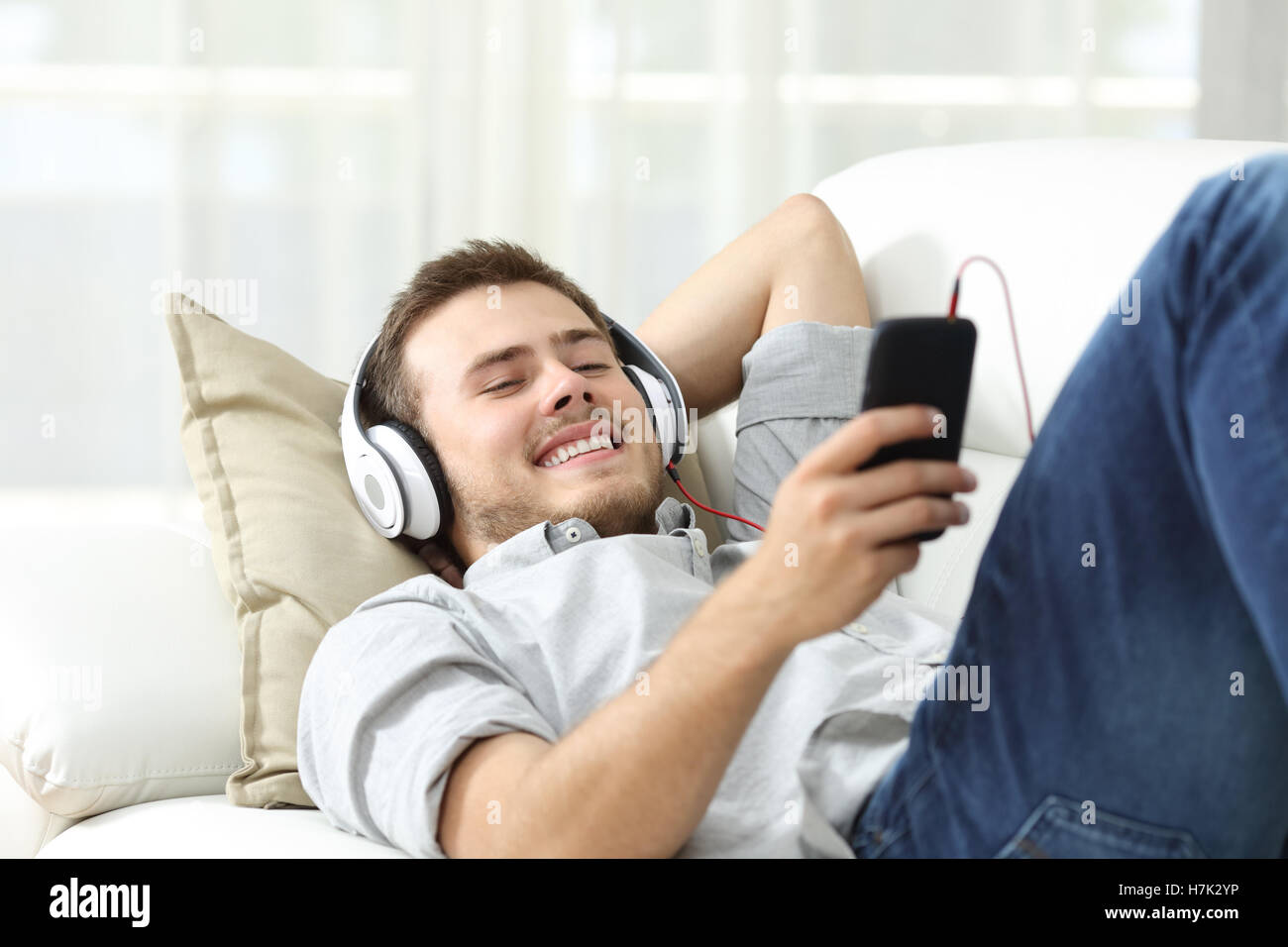 Happy man listening music lying on a sofa in the living room at home ...