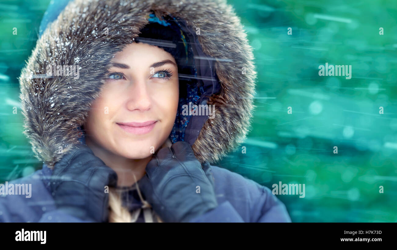 Closeup portrait of a beautiful woman enjoying snow, wearing warm coat with fur hood in snowy