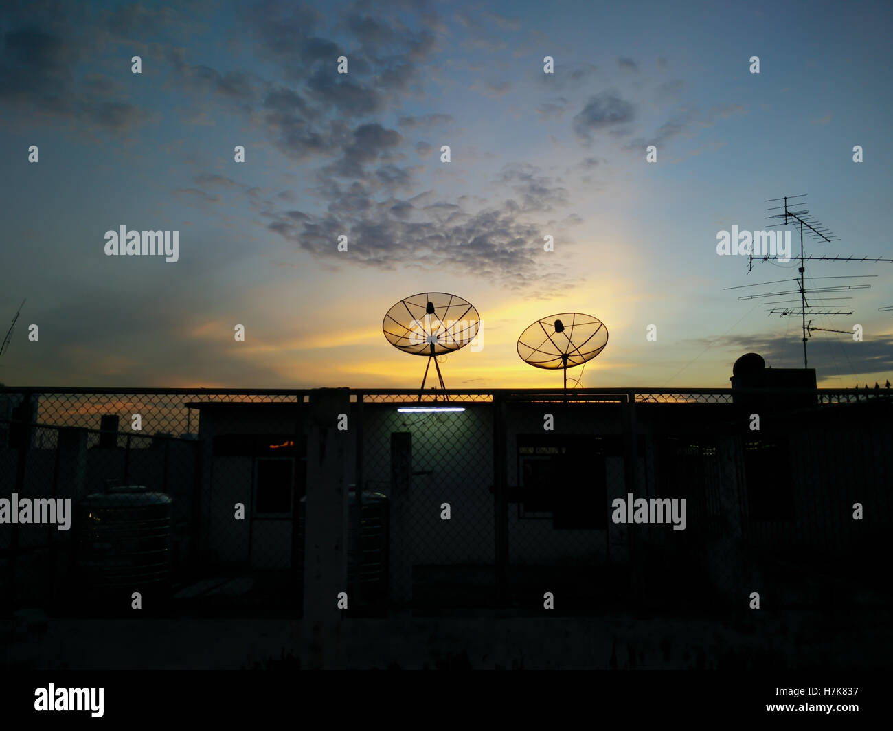 cityscape with parabolic satellite dishes at building roof and sunset background Stock Photo
