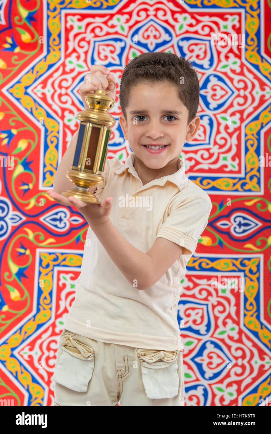 Happy Muslim Young Boy Celebrating Ramadan with Lantern over Festive Ramadan Curtain Stock Photo