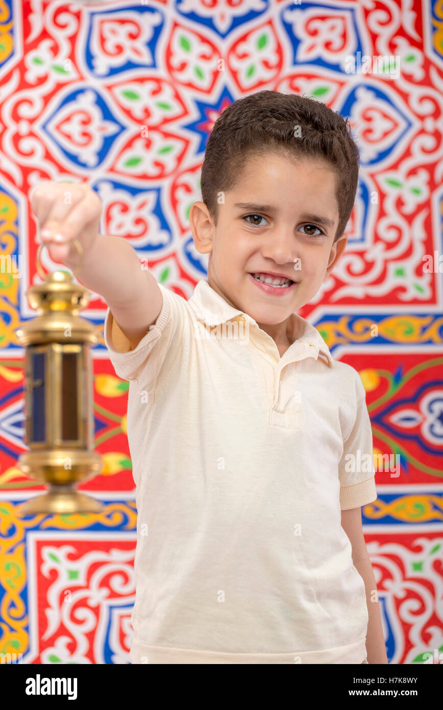 Happy Smiling Young Boy Celebrating Ramadan with Lantern over Festive Ramadan Curtain Stock Photo