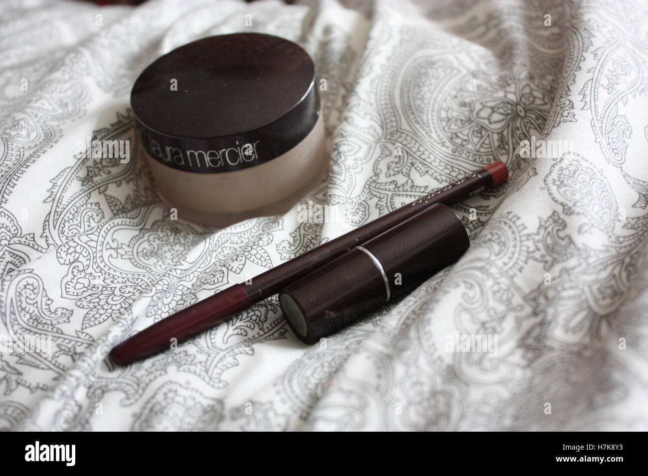 Makeup on the bed - foundation, eyeliner and a lipstick - Laura Mercier Stock Photo