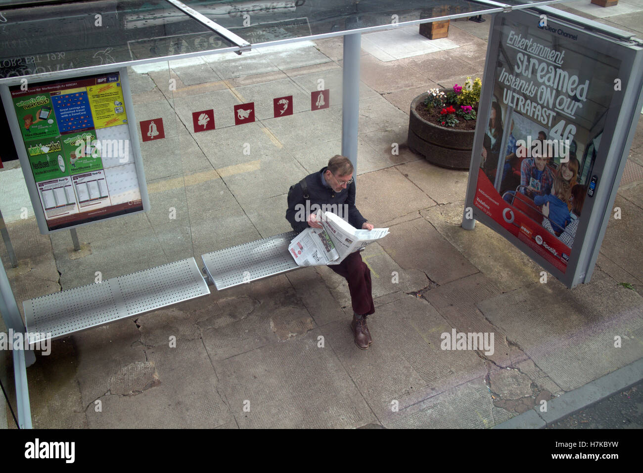 man at bus stop reading herald newspaper with adverts Stock Photo
