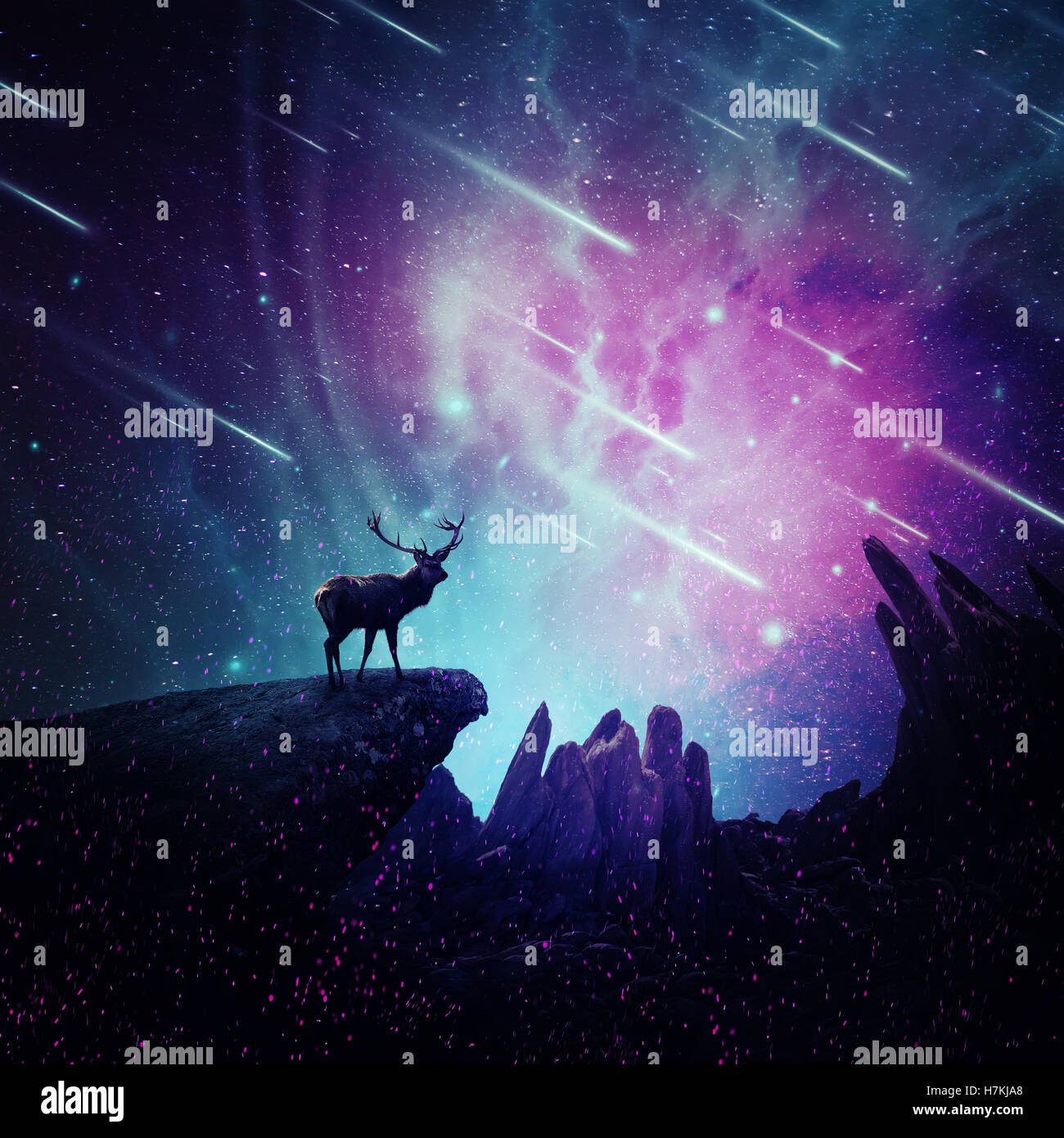 Majestic deer with long stand on the peak of a rocky hill below a wonderful night sky with falling stars and sparkles. Mystic wi Stock Photo