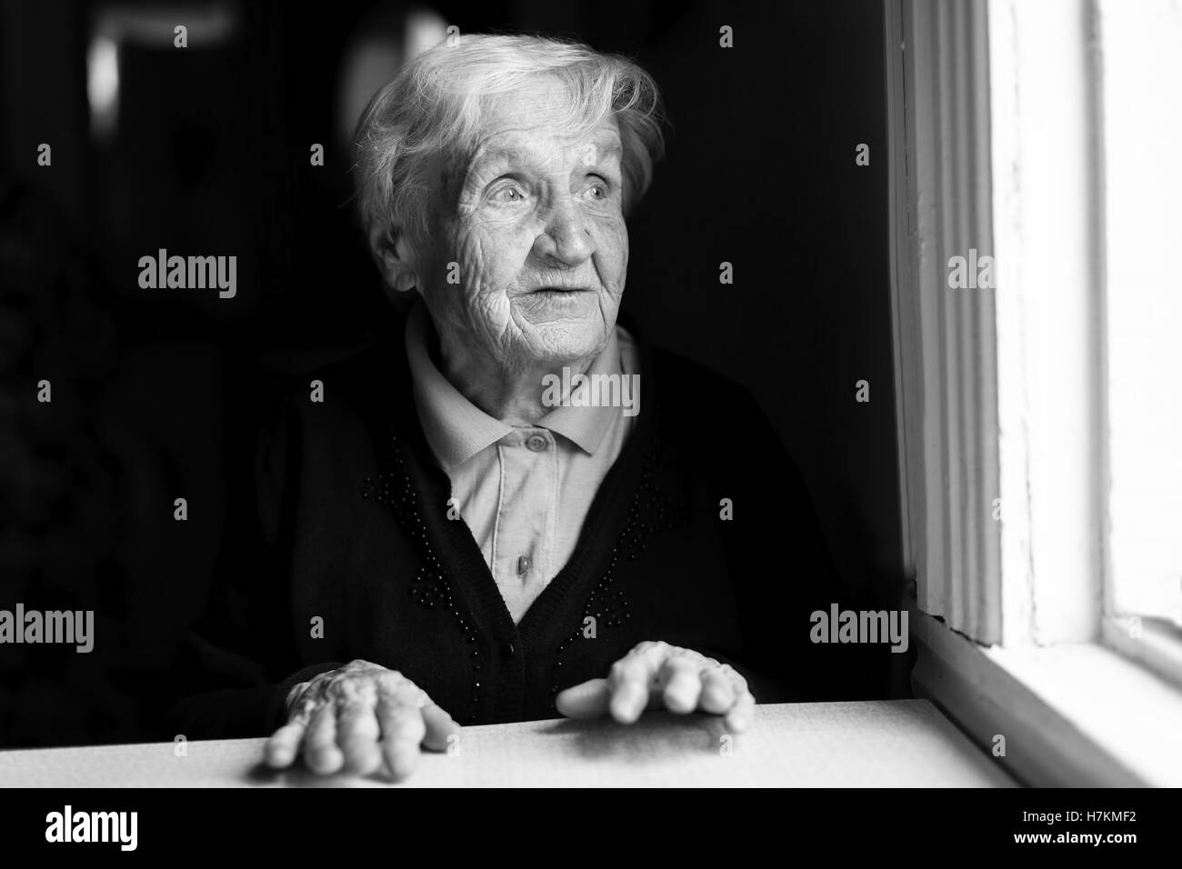 An elderly woman stares out of the window. Black and white photo. Stock Photo