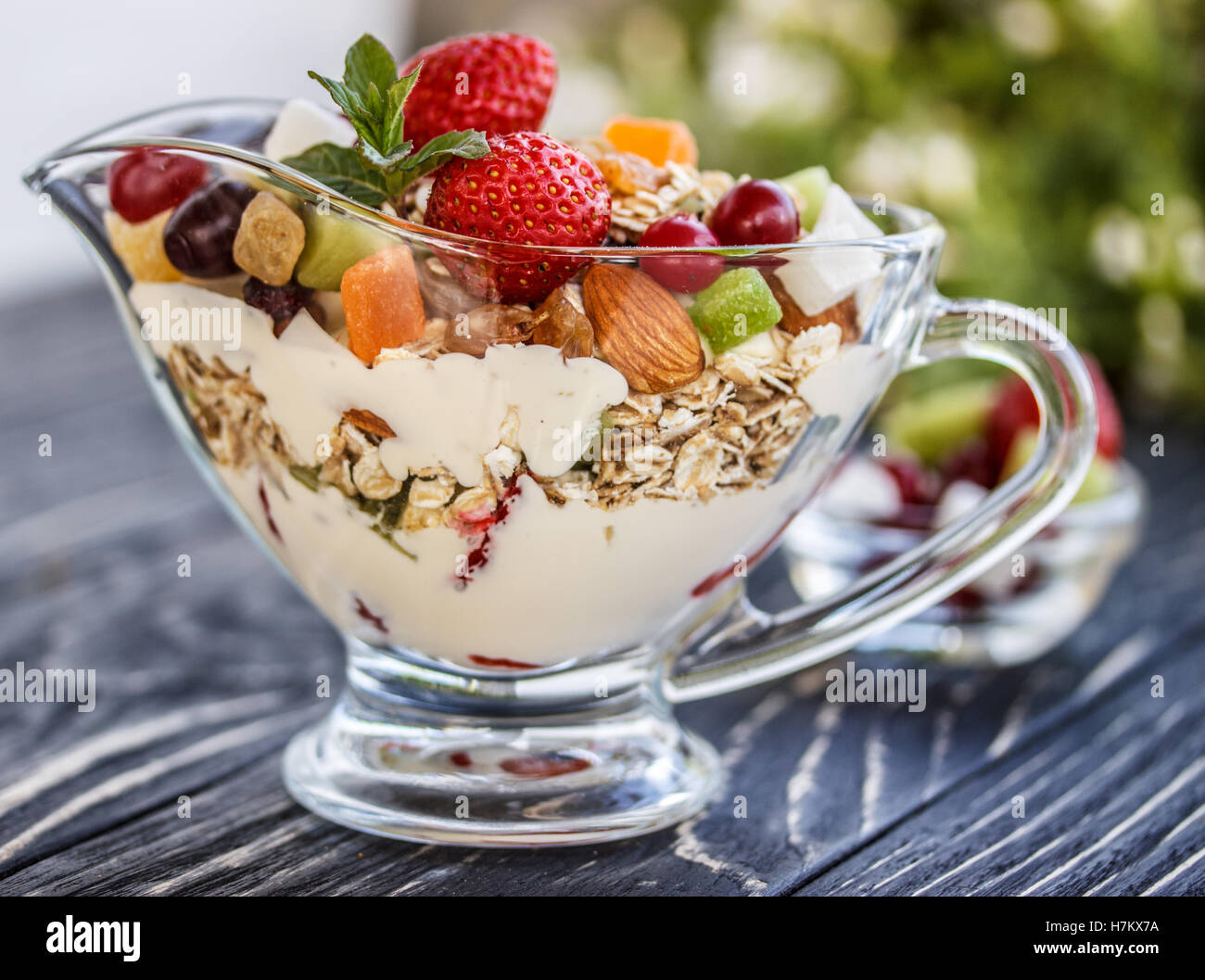 Fruit salad closeup with berries, yogurt and granola in a glass bowl on an old wooden board Stock Photo