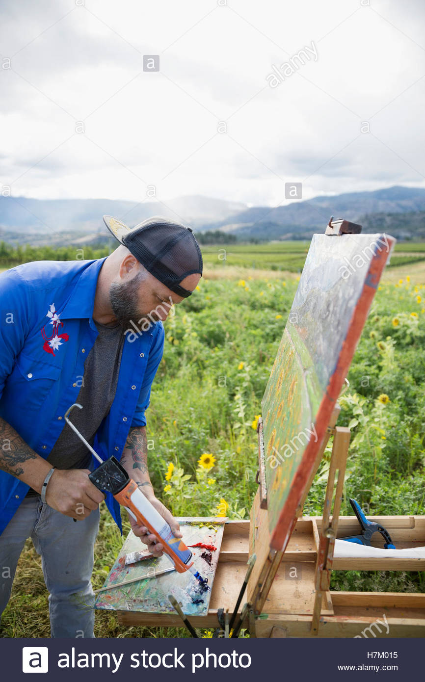 Male painter squeezing paint onto palette in rural field Stock Photo