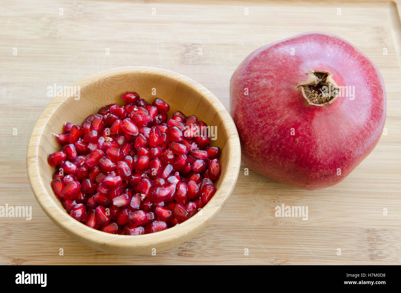 pomegranate fruit with seeds in wooden bowl on cutting board Stock Photo