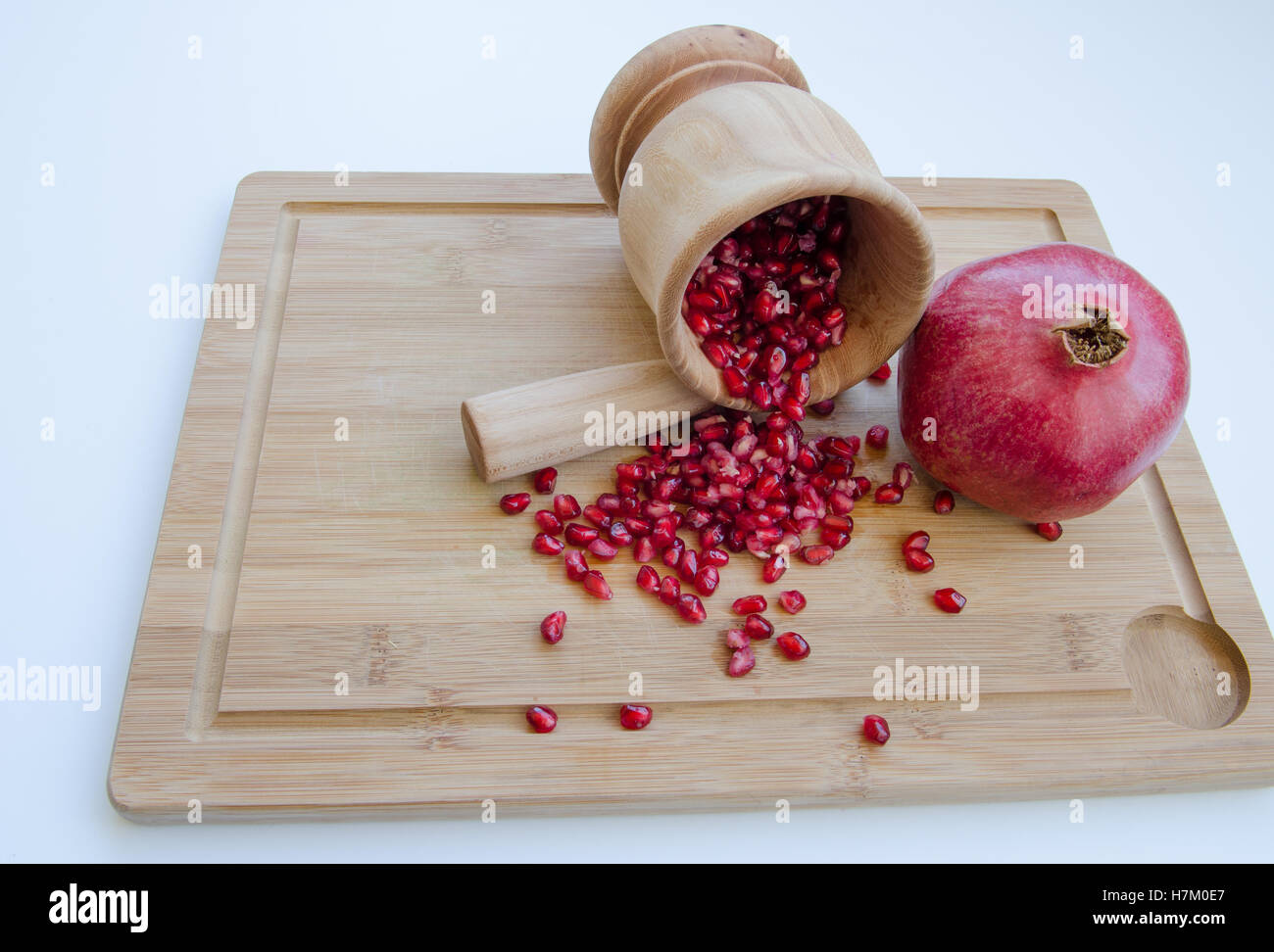 pomegranate fruit with mortar and pestle with seeds spilling on cutting board Stock Photo