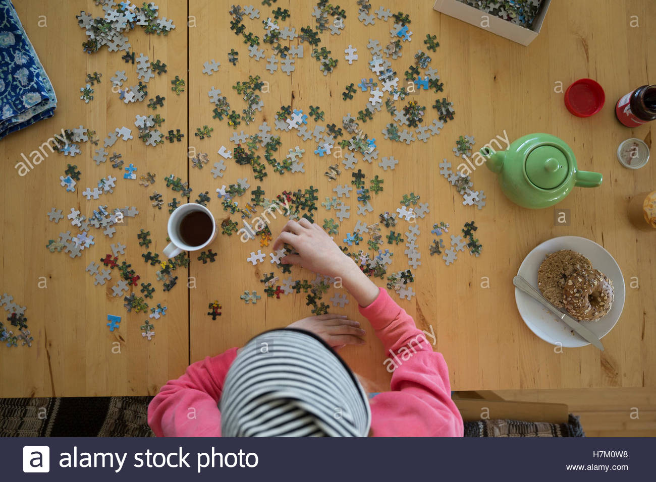 Young woman assembling jigsaw puzzle and drinking coffee at table Stock Photo
