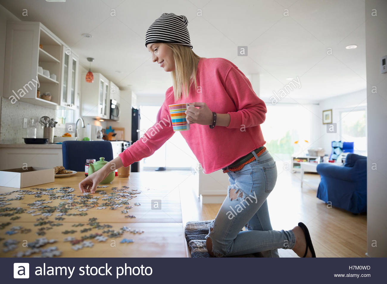 Young woman drinking coffee and assembling jigsaw puzzle at table Stock Photo