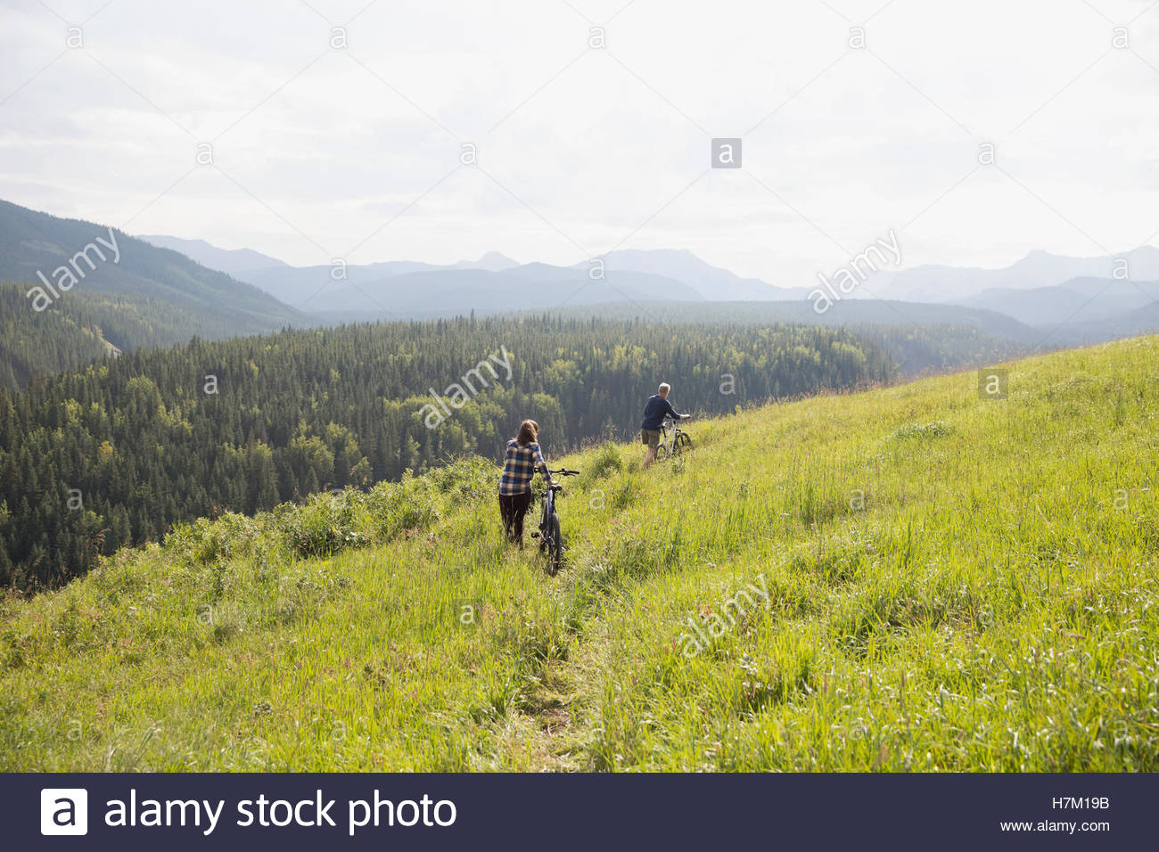 Couple walking mountain bikes in remote rural field Stock Photo