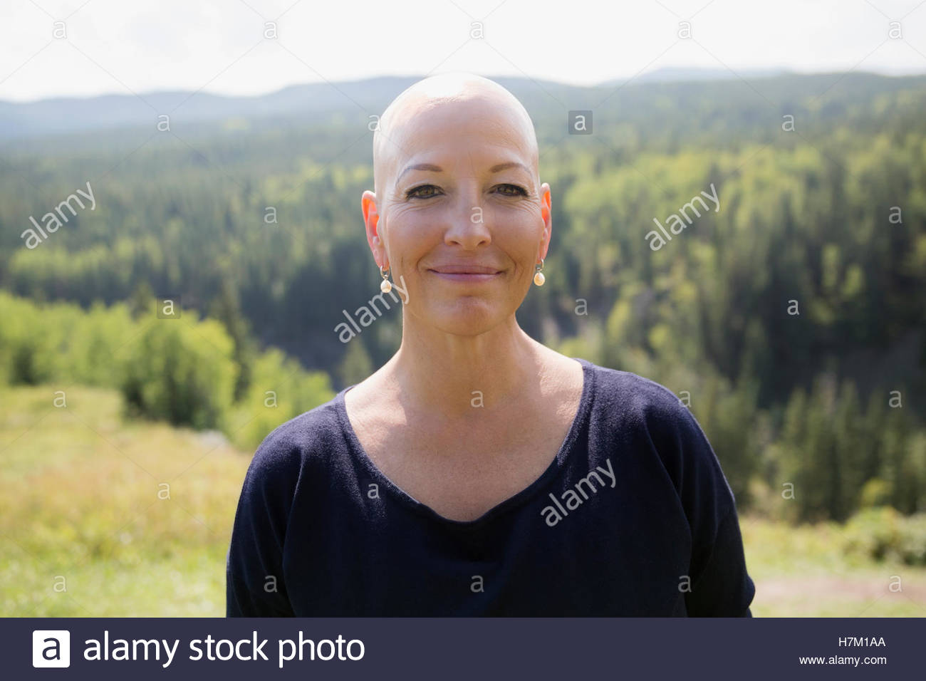 Portrait smiling female cancer survivor with shaved head at sunny remote hilltop Stock Photo