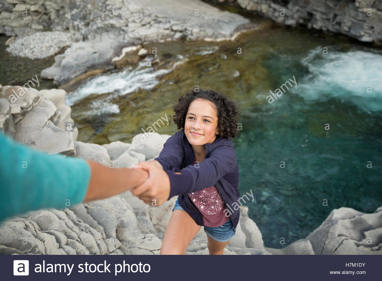 Girl climbing rocks being pulled up by helping hand Stock Photo