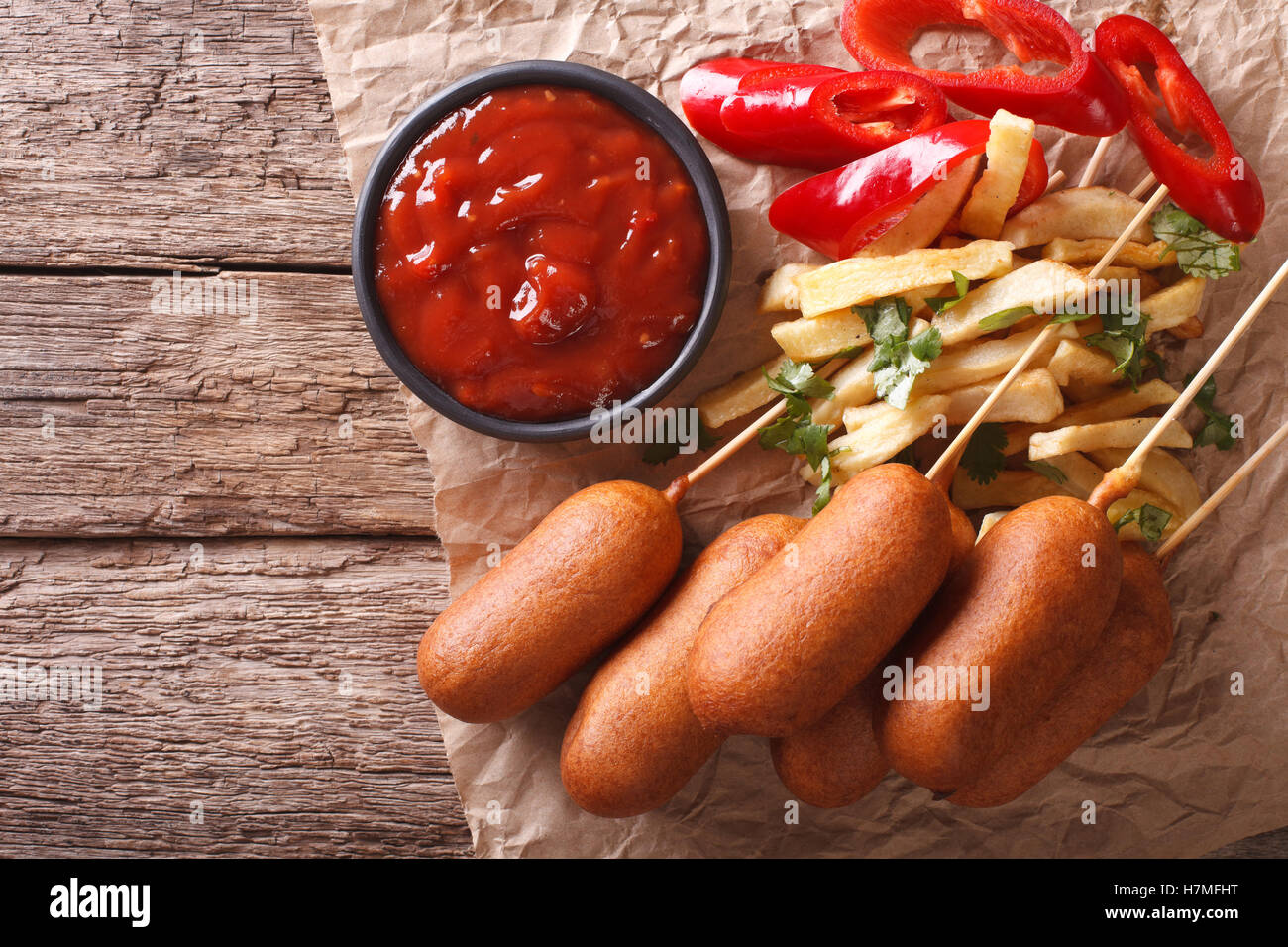 Corn dogs, french fries, pepper and ketchup on the table. Horizontal view from above Stock Photo