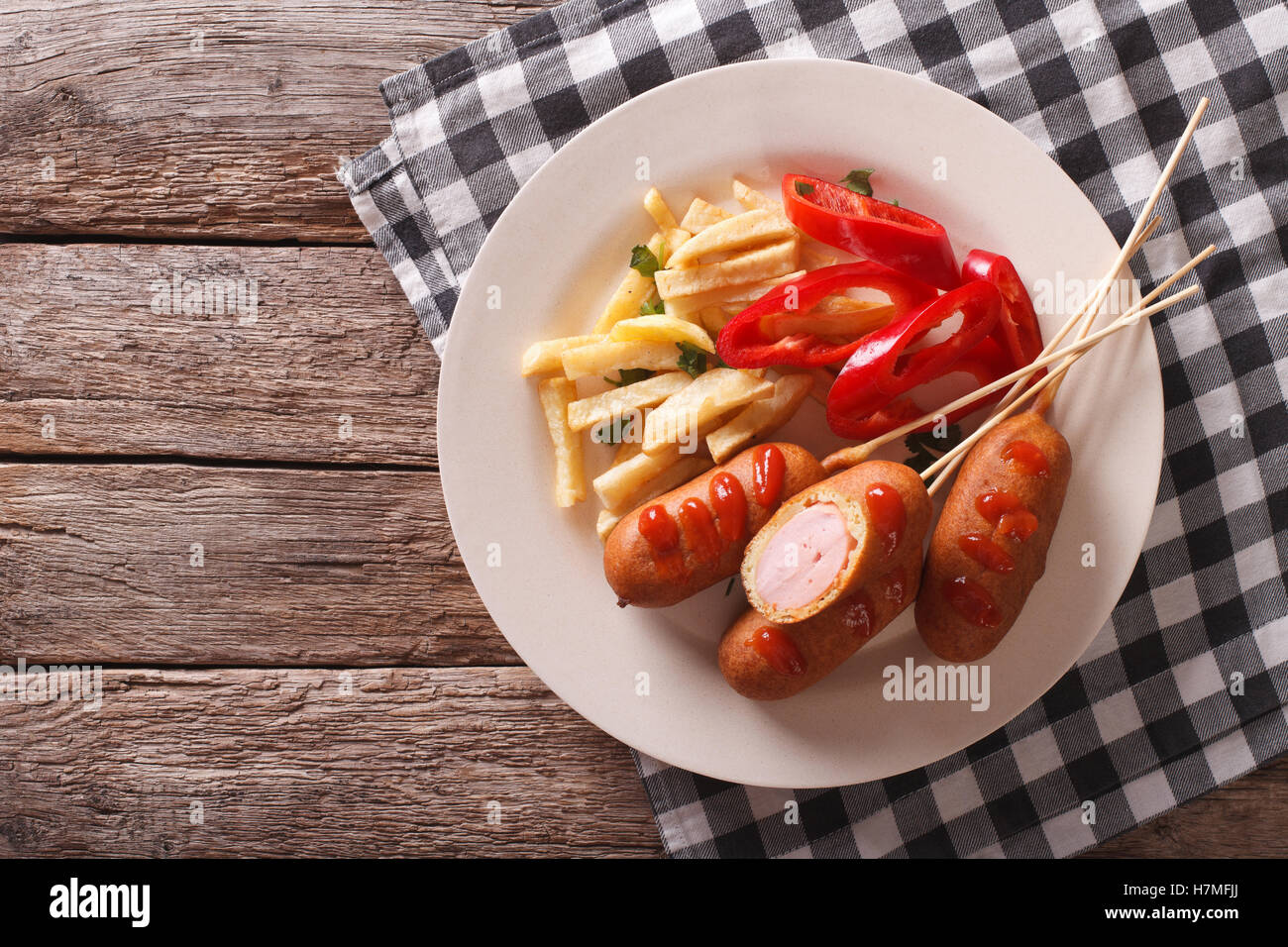 Corn dog with fries and vegetables on a plate close-up on the table. Horizontal top view Stock Photo