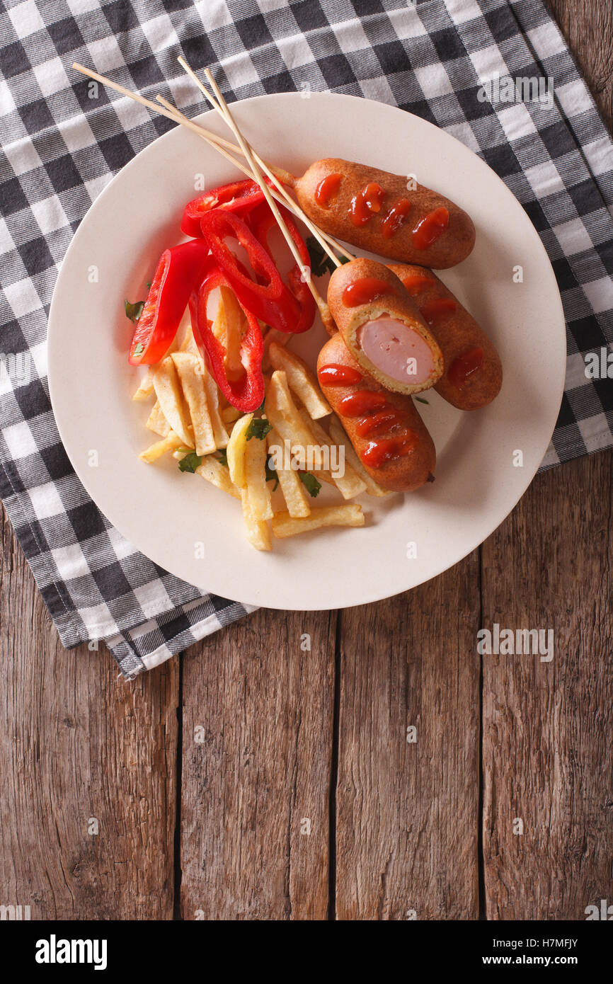 Corn dog with fries and vegetables on a plate close-up on the table. vertical top view Stock Photo