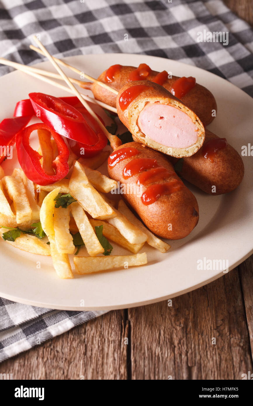 Corn dog, french fries and vegetables on a plate close-up on the table. Vertical Stock Photo