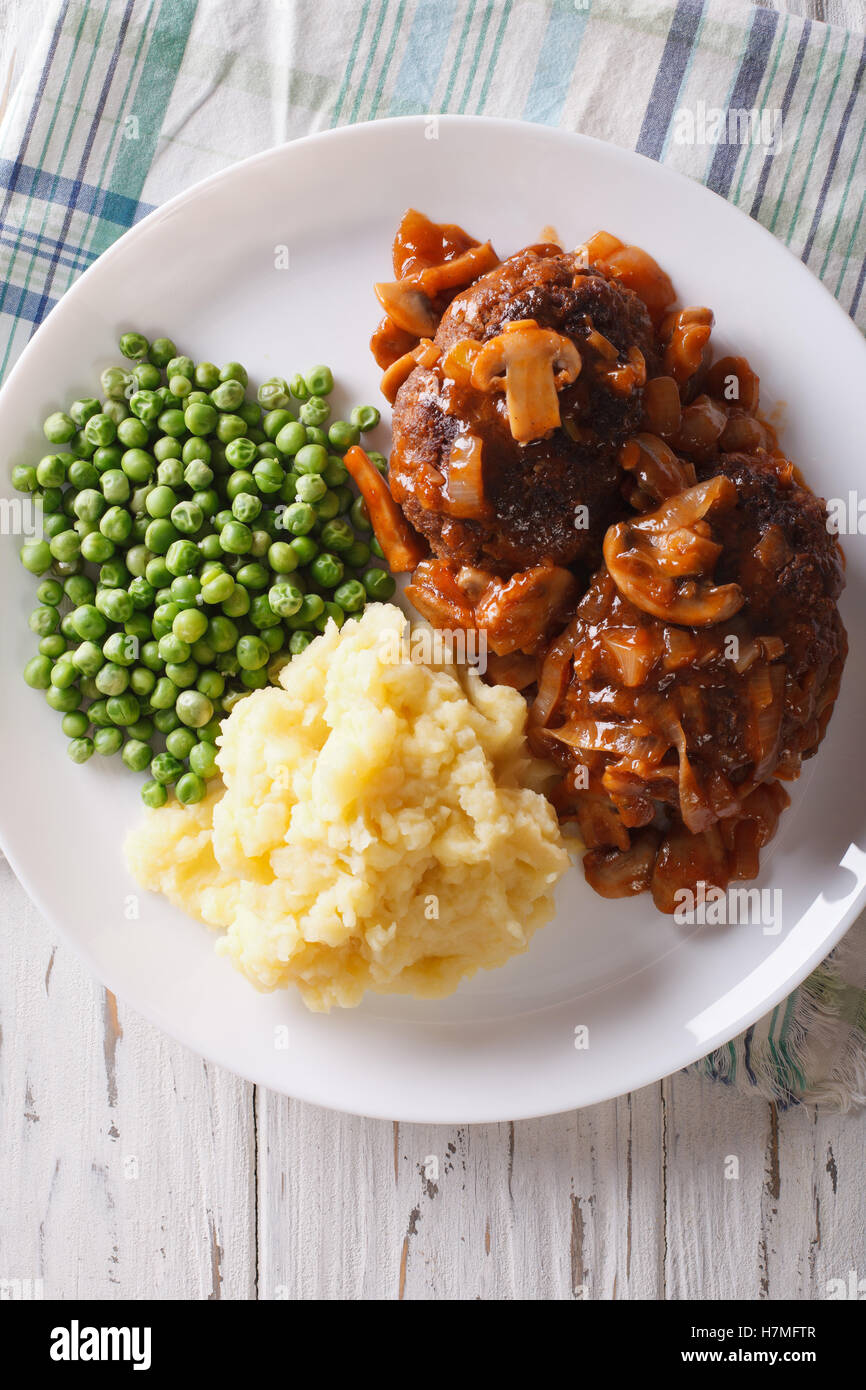 Salisbury steak with potatoes and green peas close-up on a plate on the table. vertical view from above Stock Photo