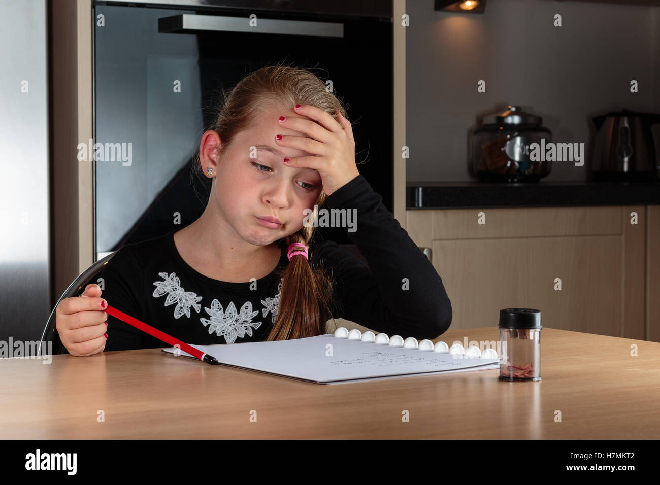 Young girl doing homework at home at the kitchen table sighing. Stock Photo