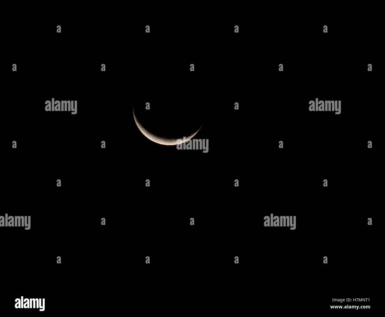 sliver of silver crescent moon with lunar landscape features visible in inky black sky in