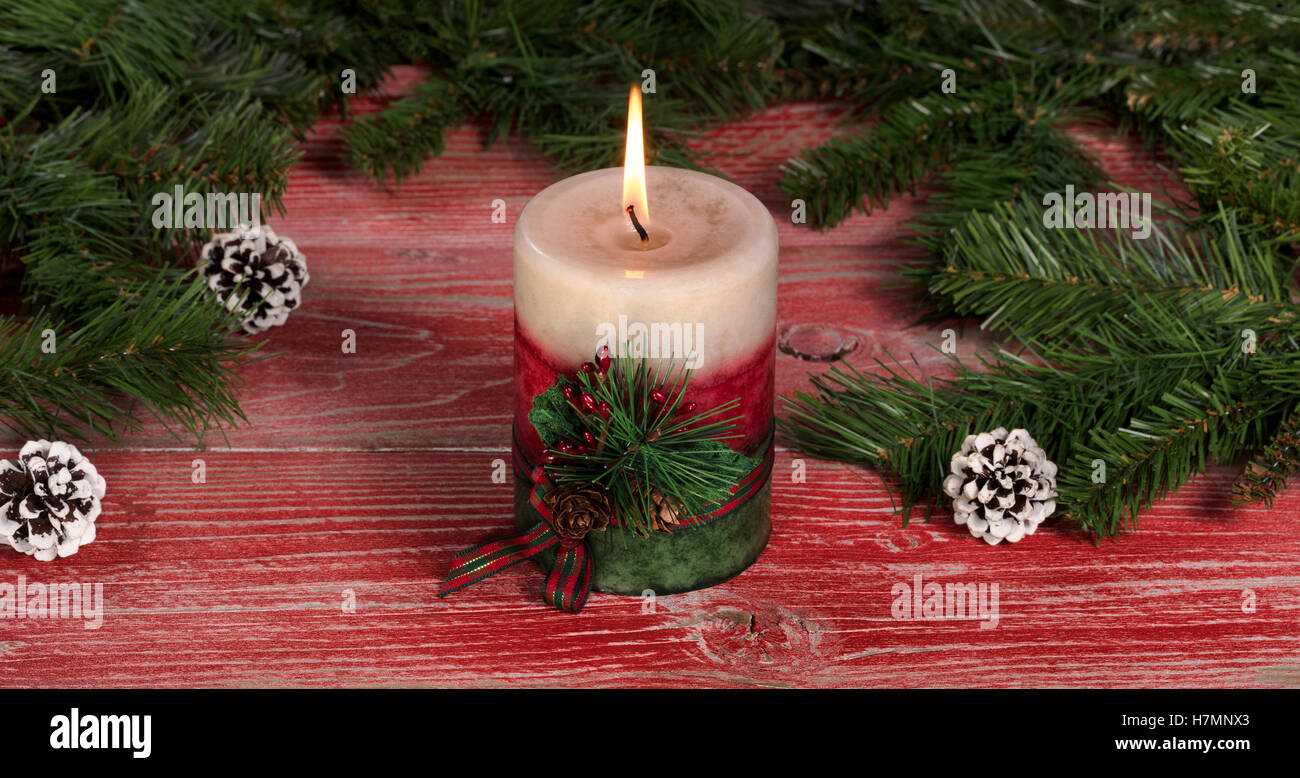 Close up of a burning candle with fir branches and pine cones on rustic red wooden boards for Christmas concept. Stock Photo