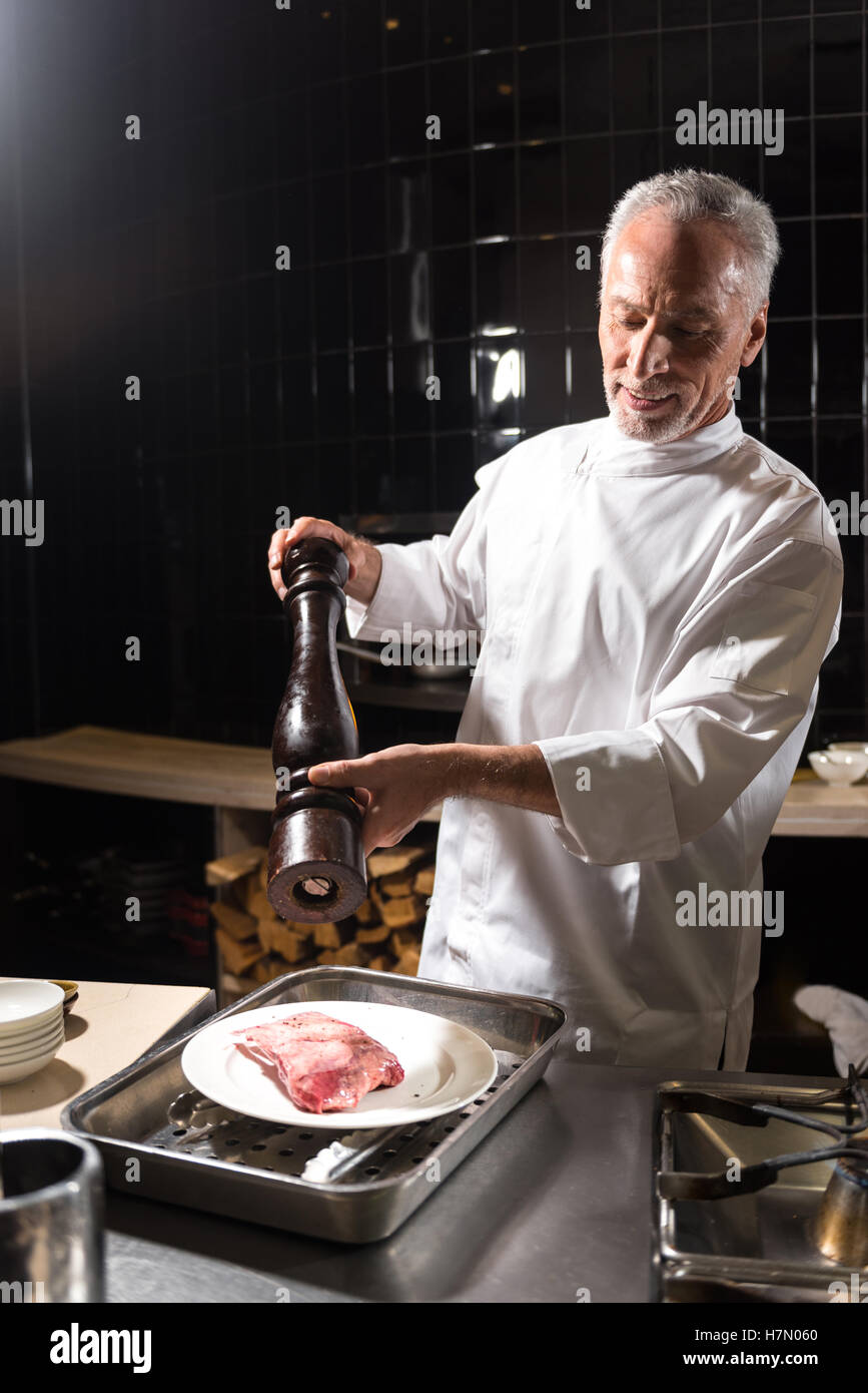 Bearded happy chef putting salt on the steak Stock Photo Alamy