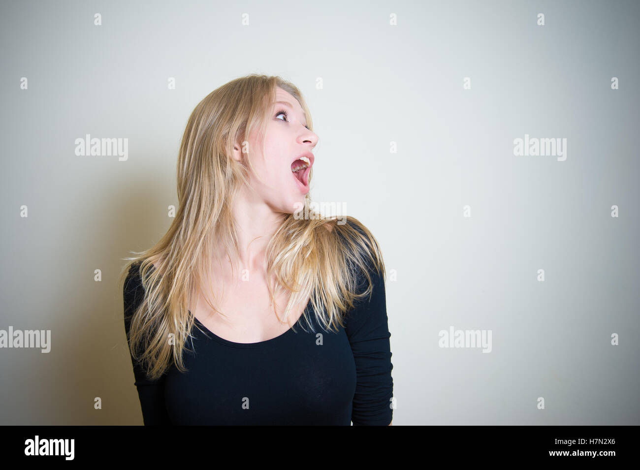 Young blonde woman, black shirt, astonished crying at her left with open mouth on white background Stock Photo