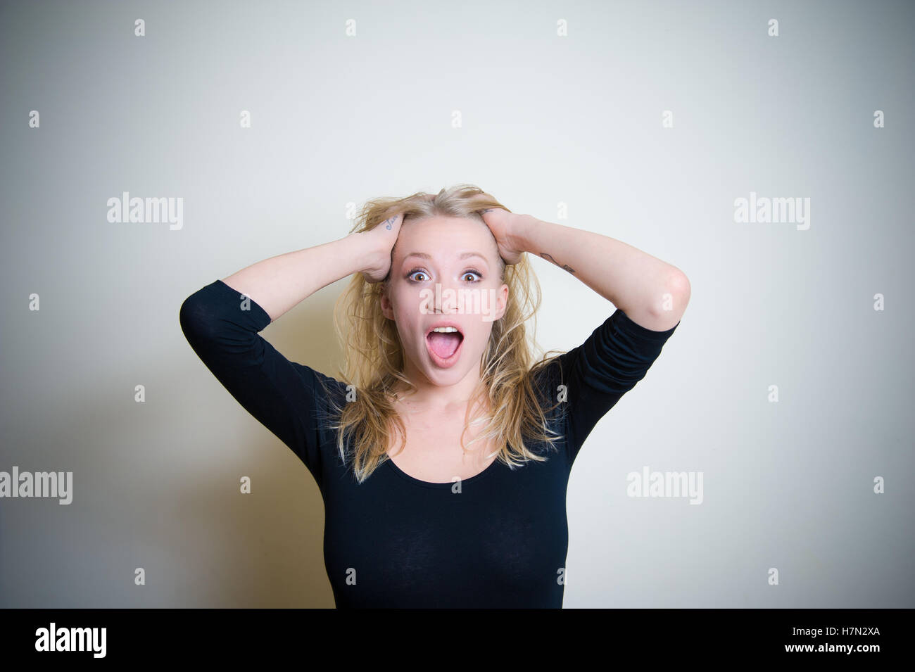 Young blond woman, black shirt, astonished crying with open mouth looking at camera on white background Stock Photo