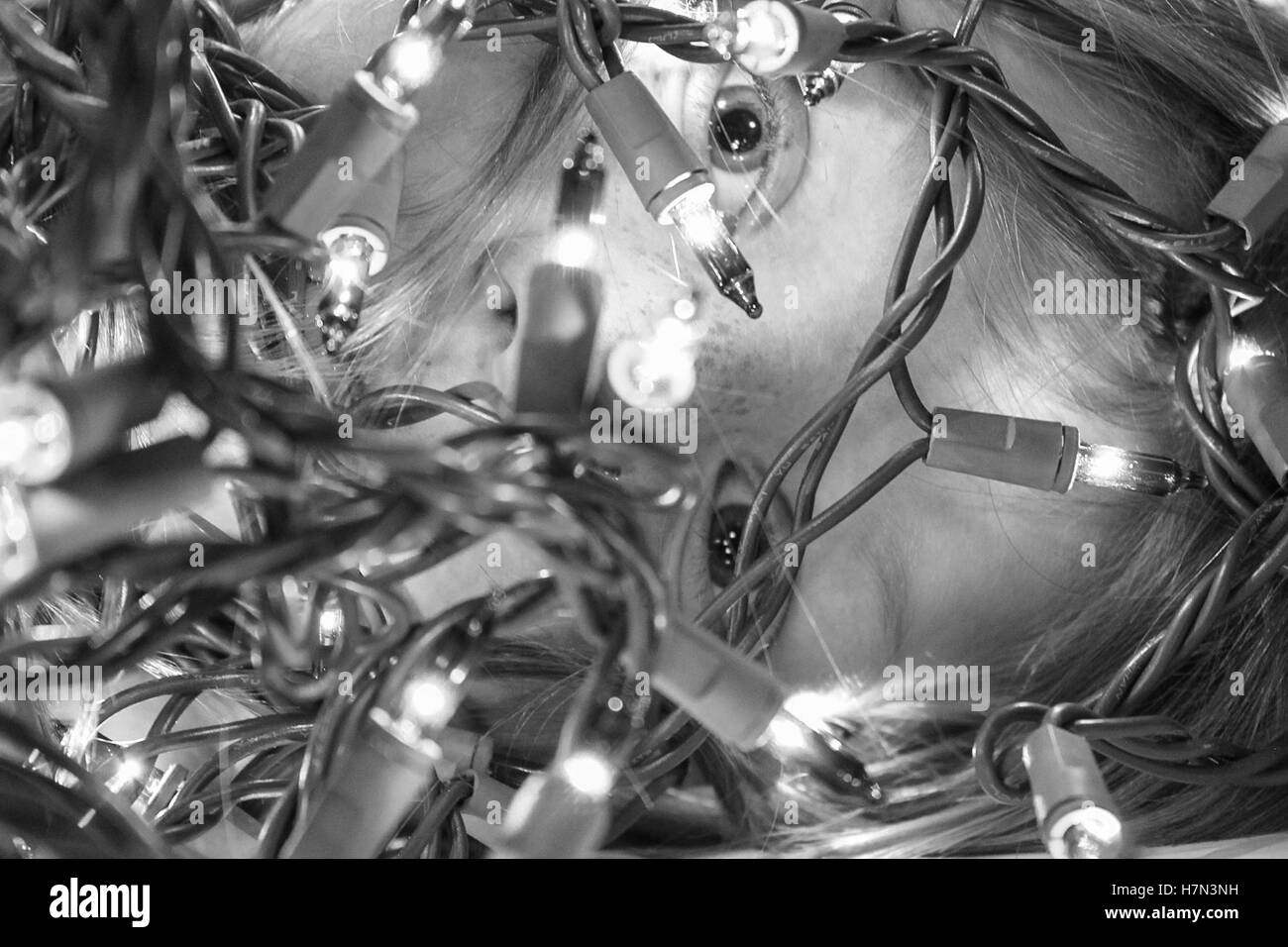 close up of child peeking through christmas lights, black and white Stock Photo