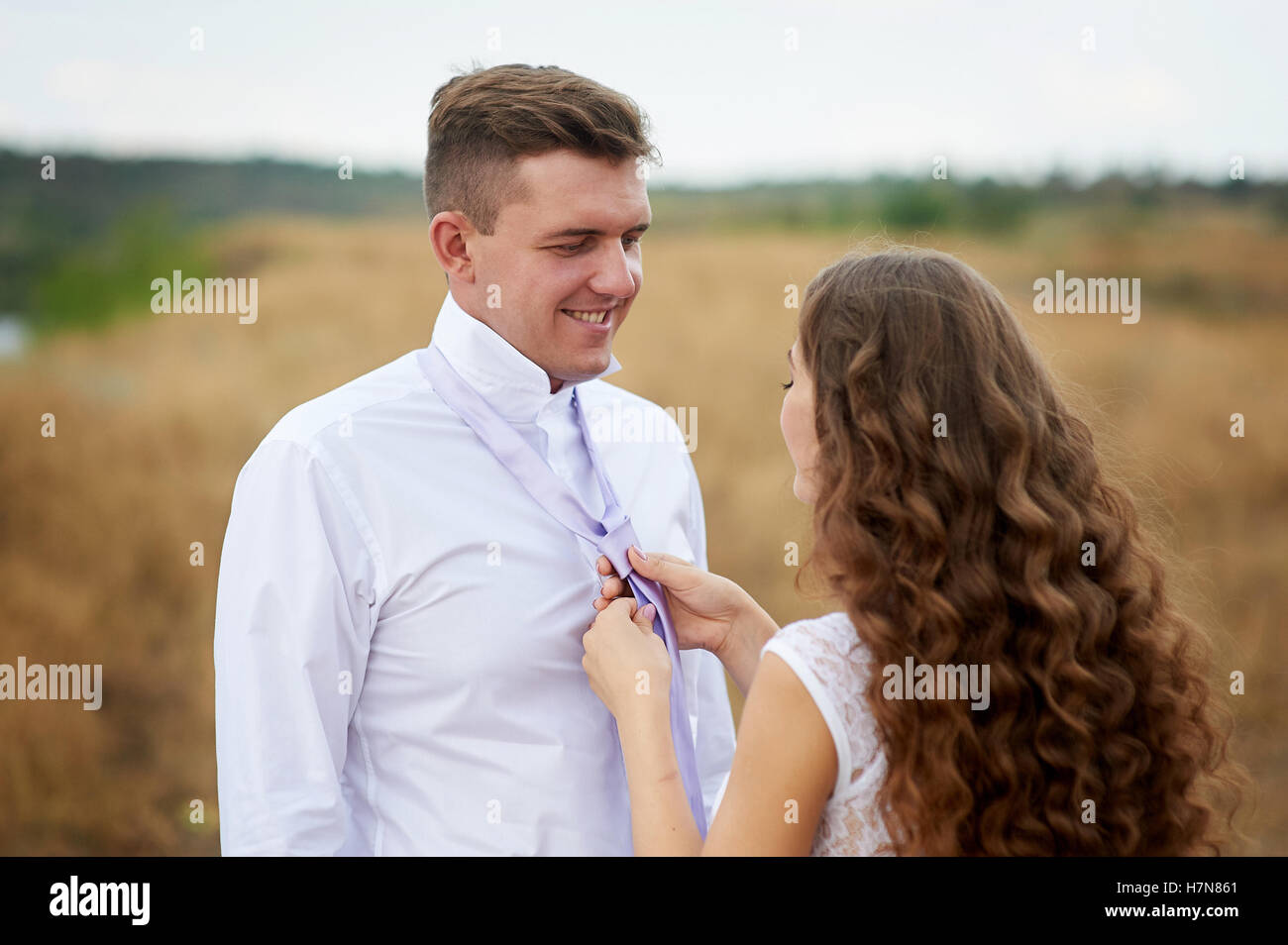 bride dress for groom his tie on the nature in field Stock Photo
