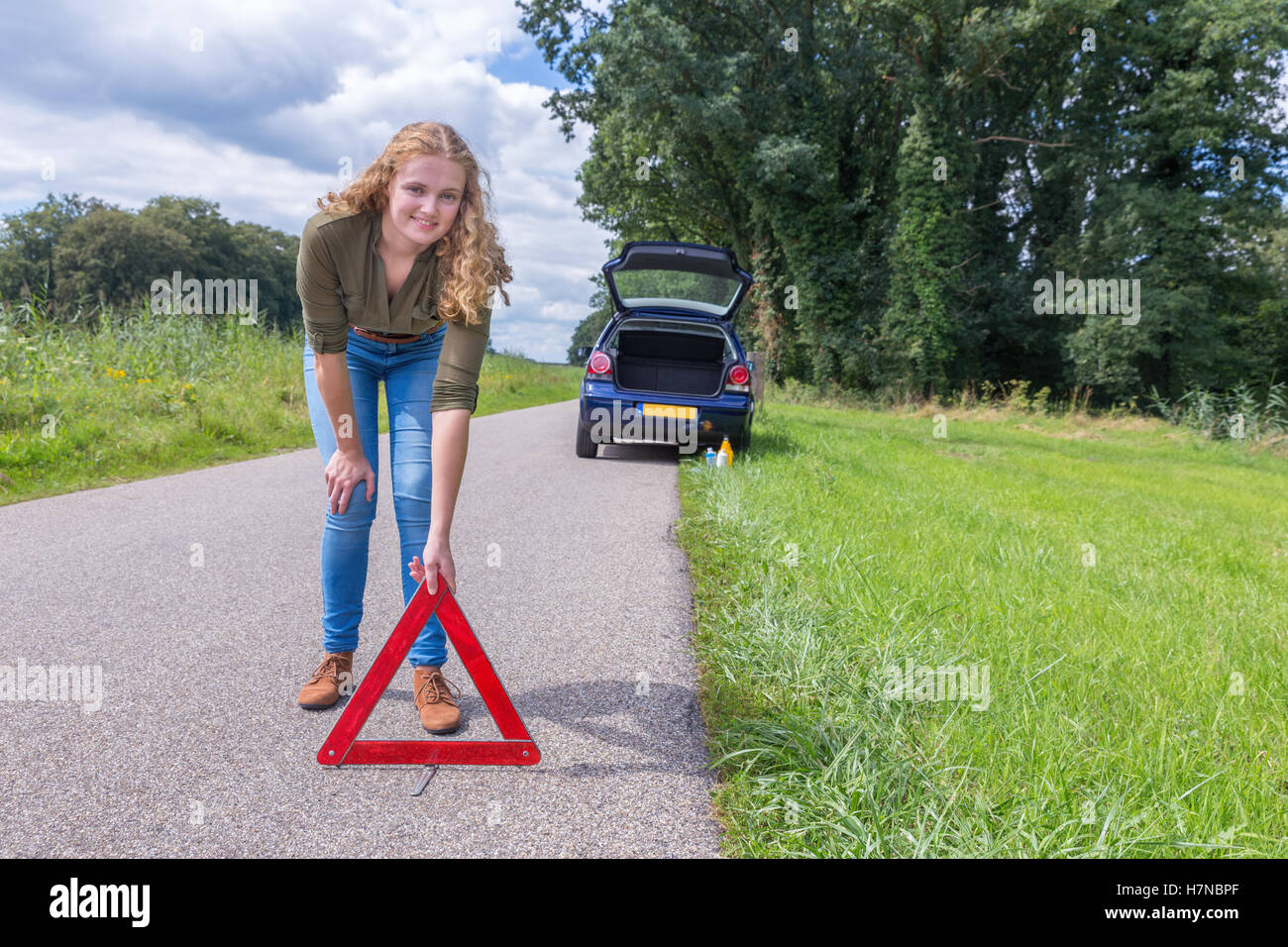 European woman placing hazard warning triangle on rural road Stock Photo