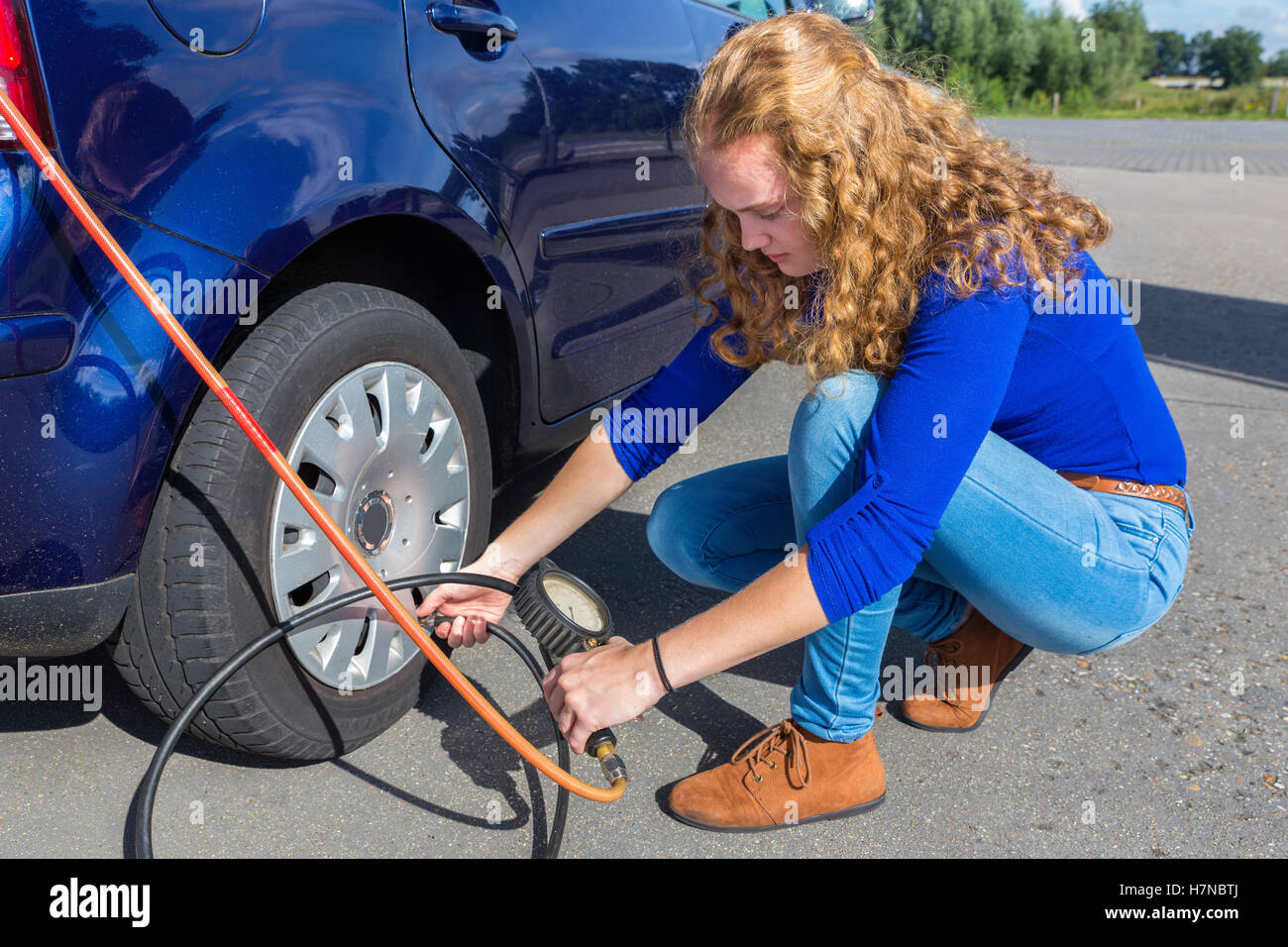 Female driver checking air pressure of car tire outdoors Stock Photo