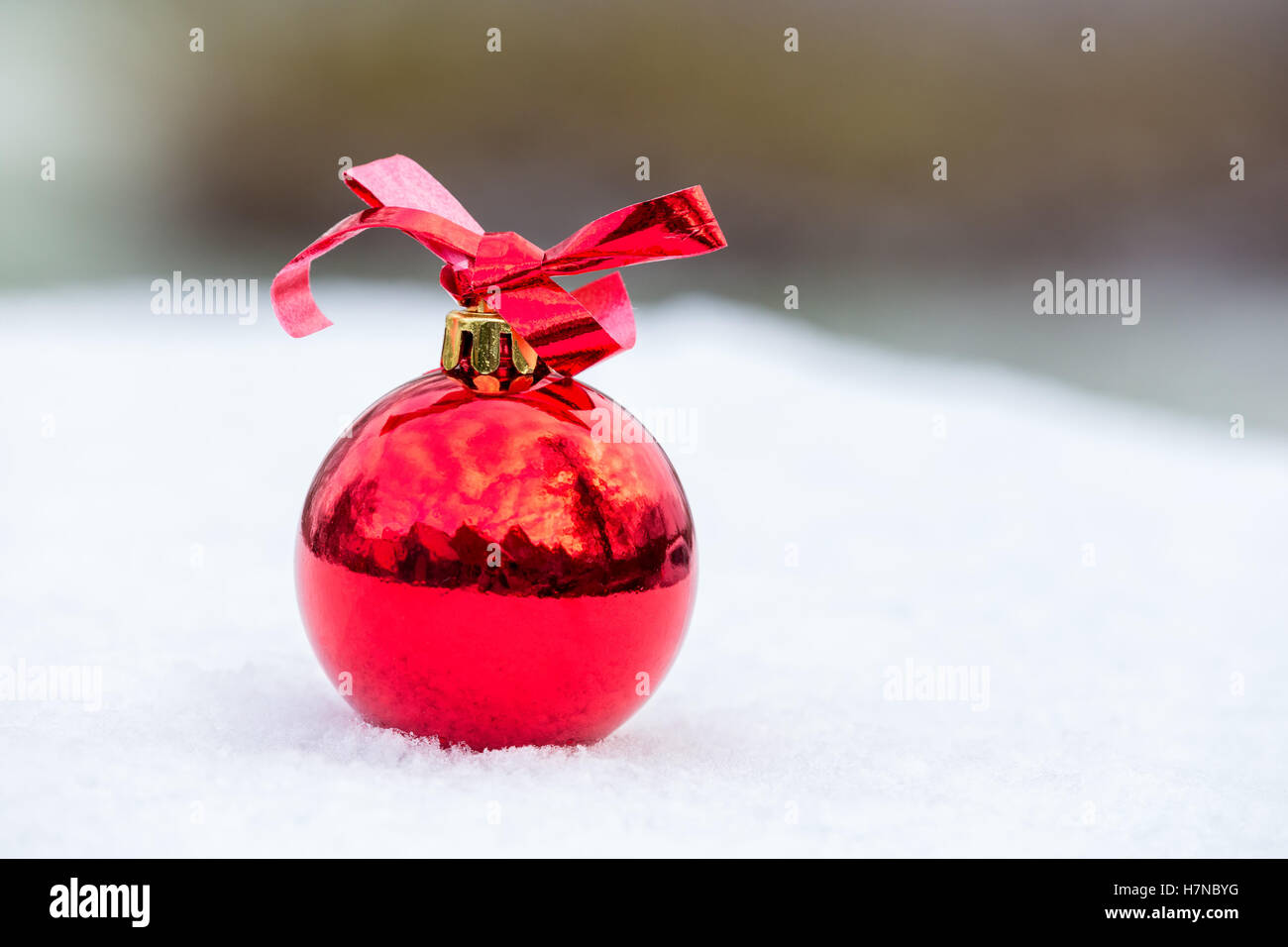 One shiny red christmas ball with bow outside in winter snow Stock Photo