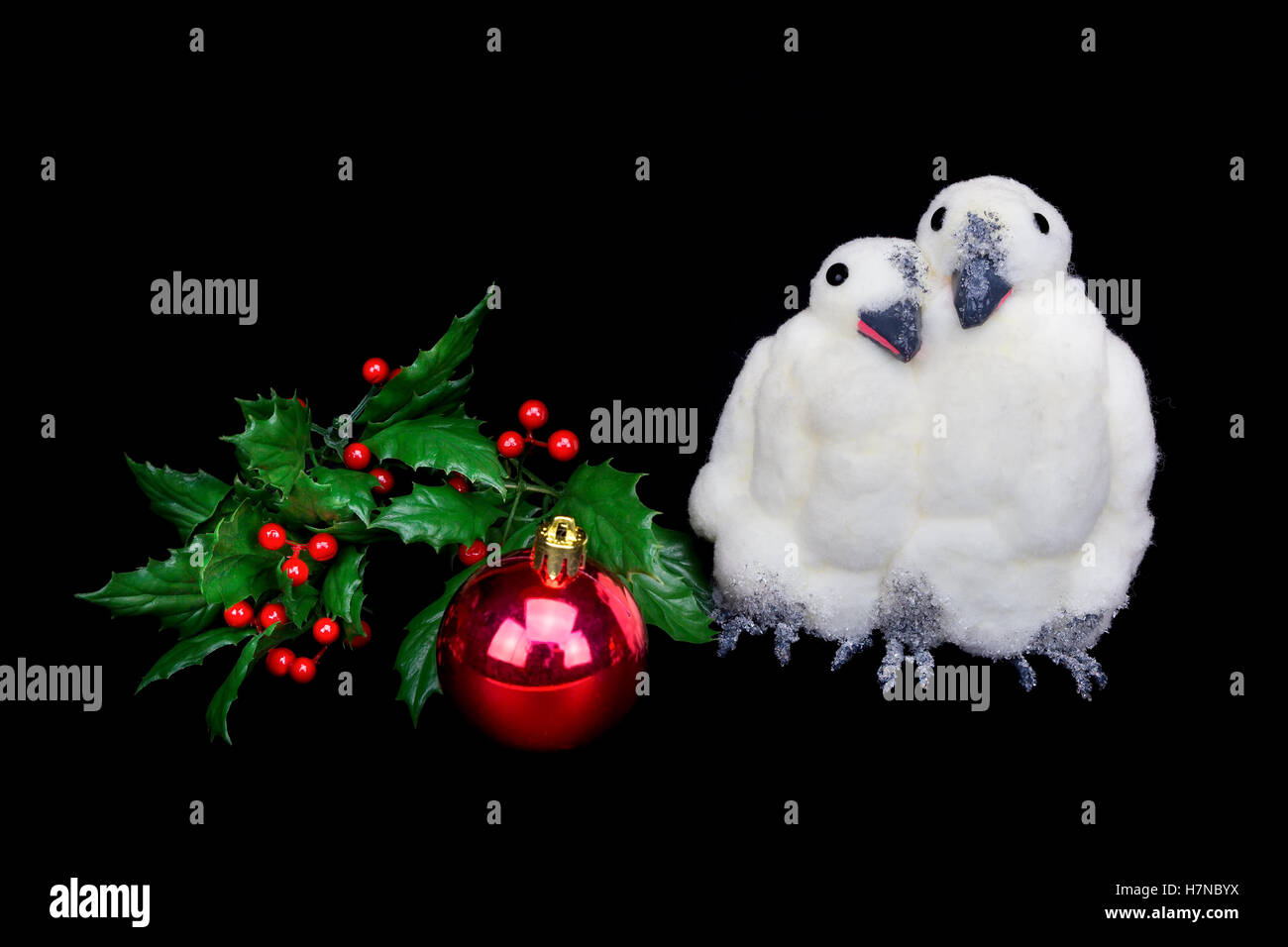Two penguin figures together with baubles and holly berries isolated on black background Stock Photo