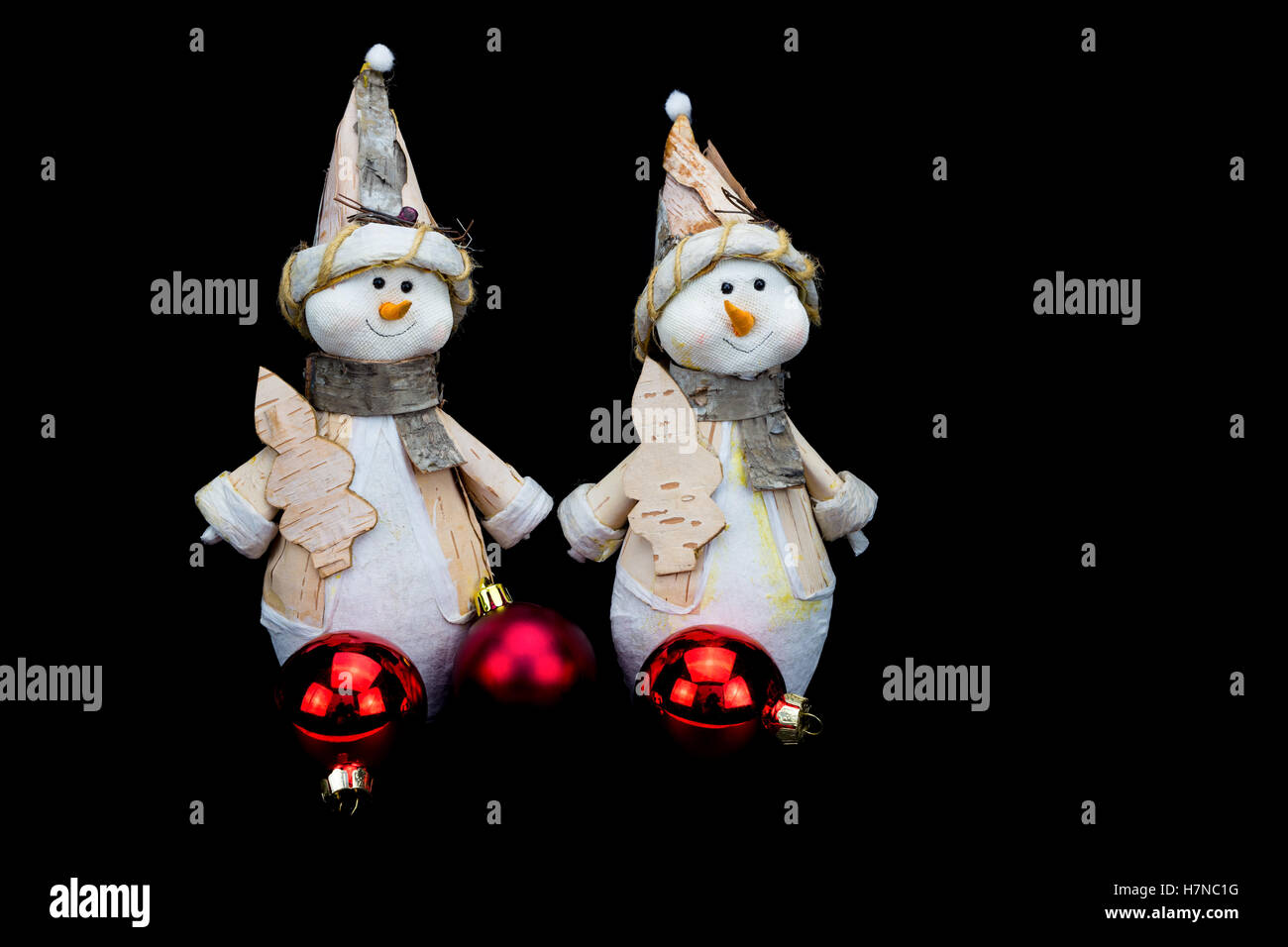 Two snowmen figurines with red baubles on black Stock Photo