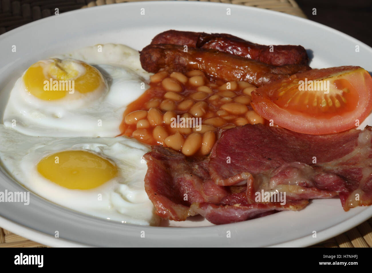 English breakfast served by a hotel in Malta - two fried eggs, rashers of local bacon, two sausages, tomato, baked beans. Stock Photo