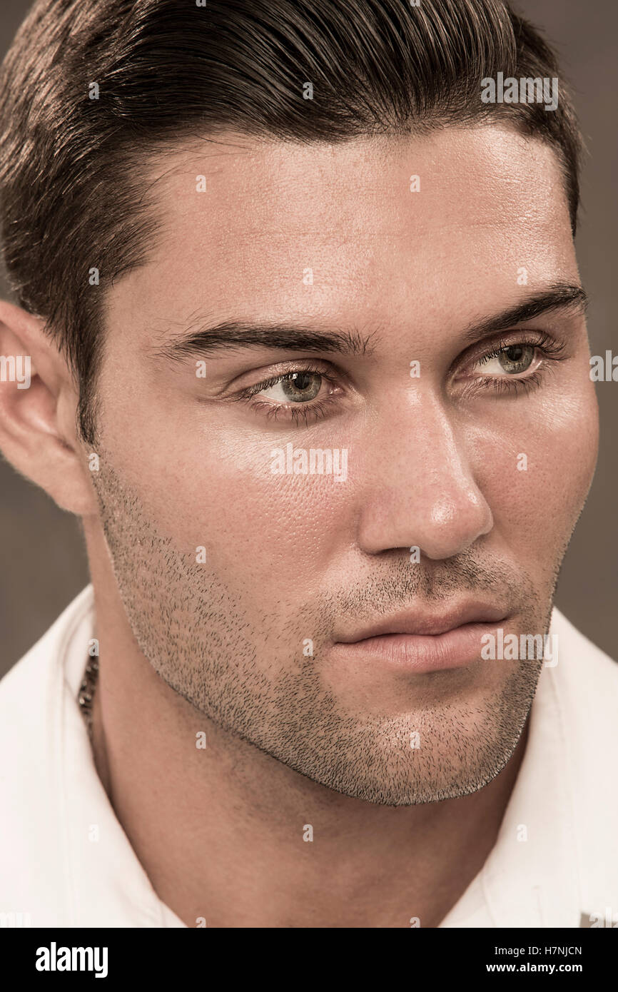 Handsome young man with beard stubble and modern hairstyle in serious studio portrait with subdued amber tones, looking aside. Stock Photo