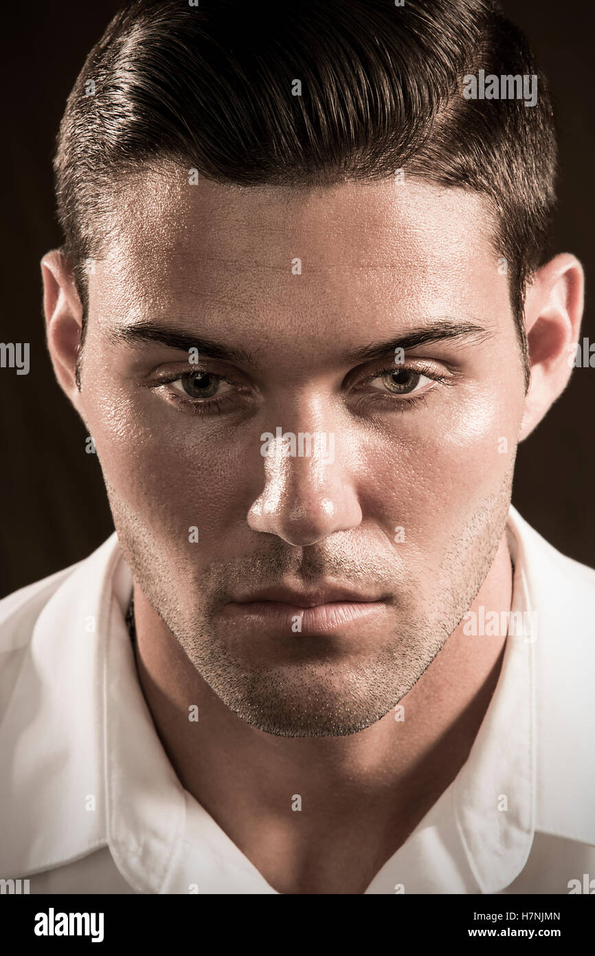 Handsome young man with dark beard stubble and modern hairstyle in serious head and shoulders studio portrait with amber tones. Stock Photo